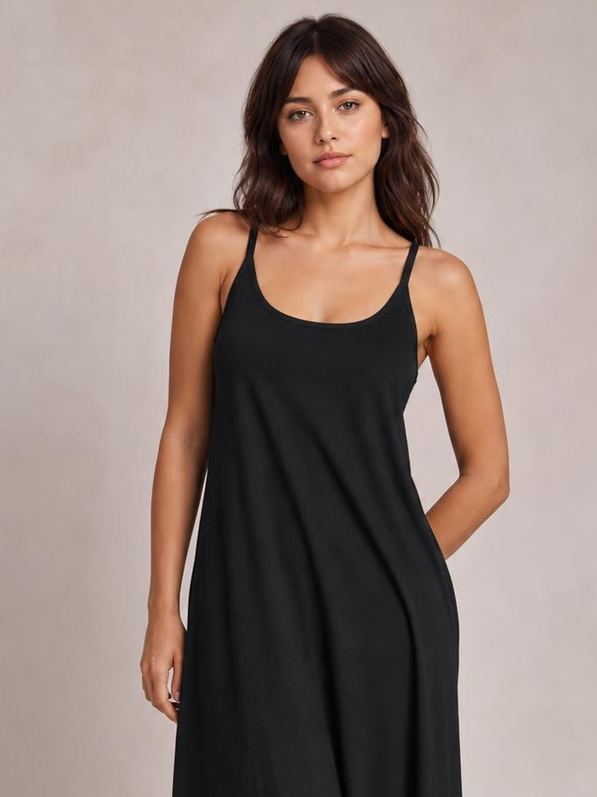 Model poses in a black plus-size maxi dress with a scoop neck, thin spaghetti straps, and a loose, flowing silhouette.