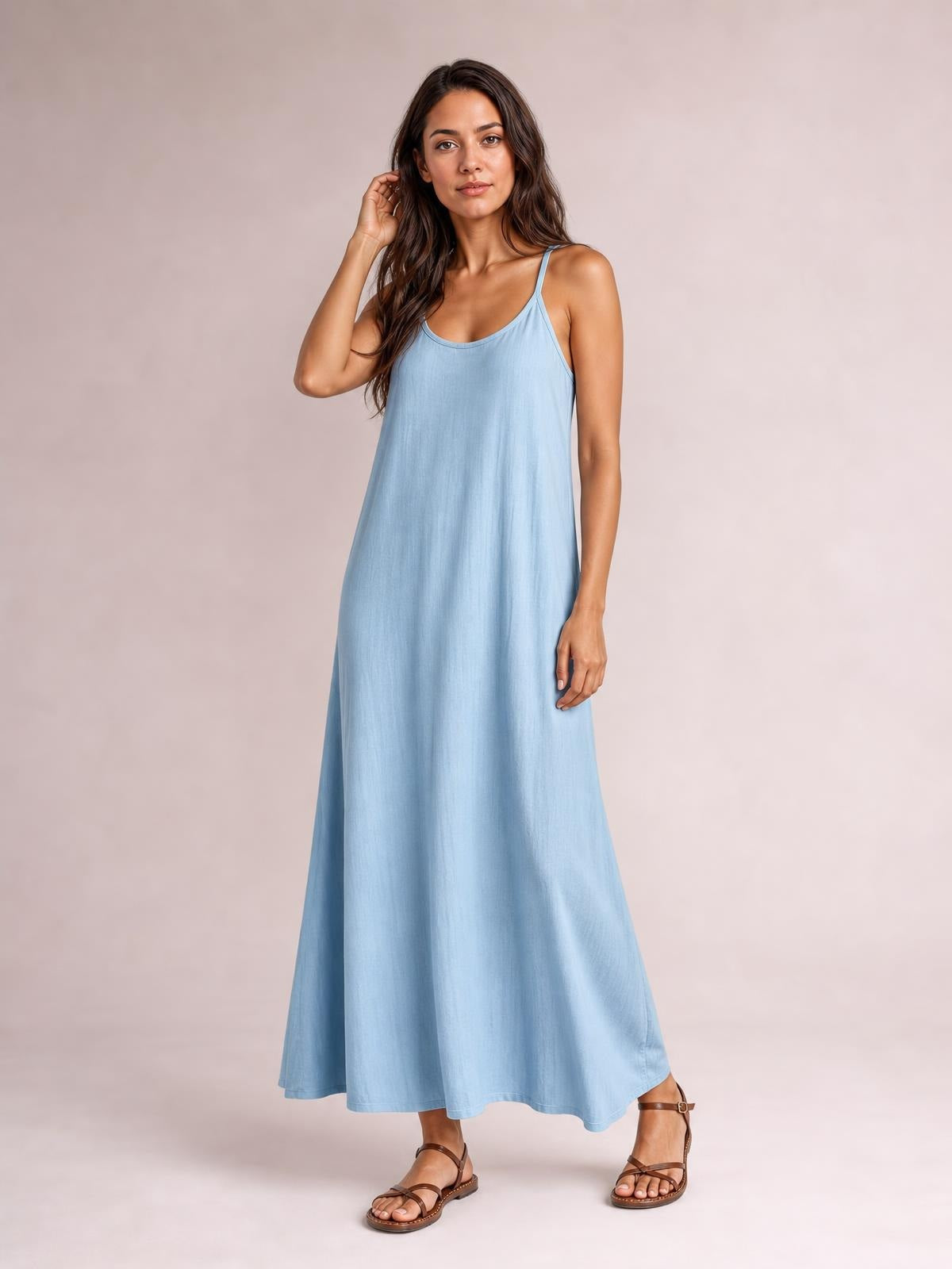 Model poses in a light blue scoop-neck maxi dress with thin spaghetti straps, a relaxed flowing silhouette, and a gently curved hem.
