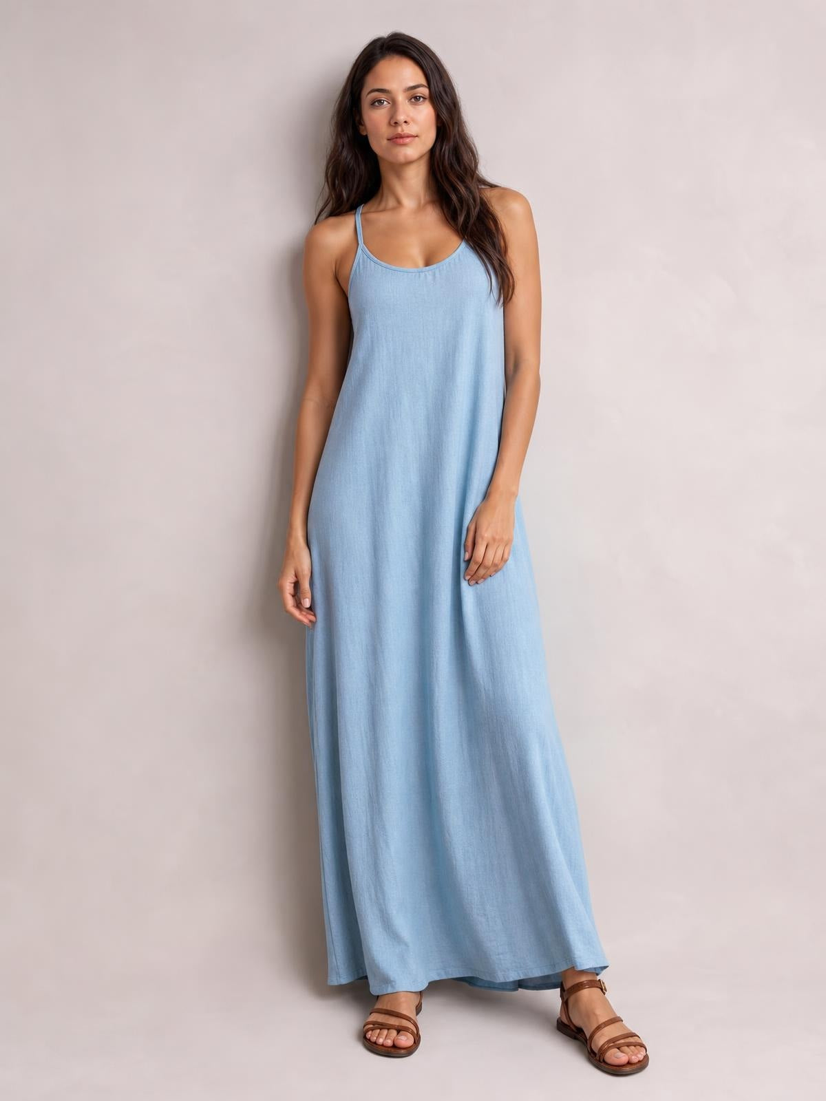 Model stands in a light blue scoop-neck maxi dress with slim spaghetti straps and a relaxed, flowing silhouette.