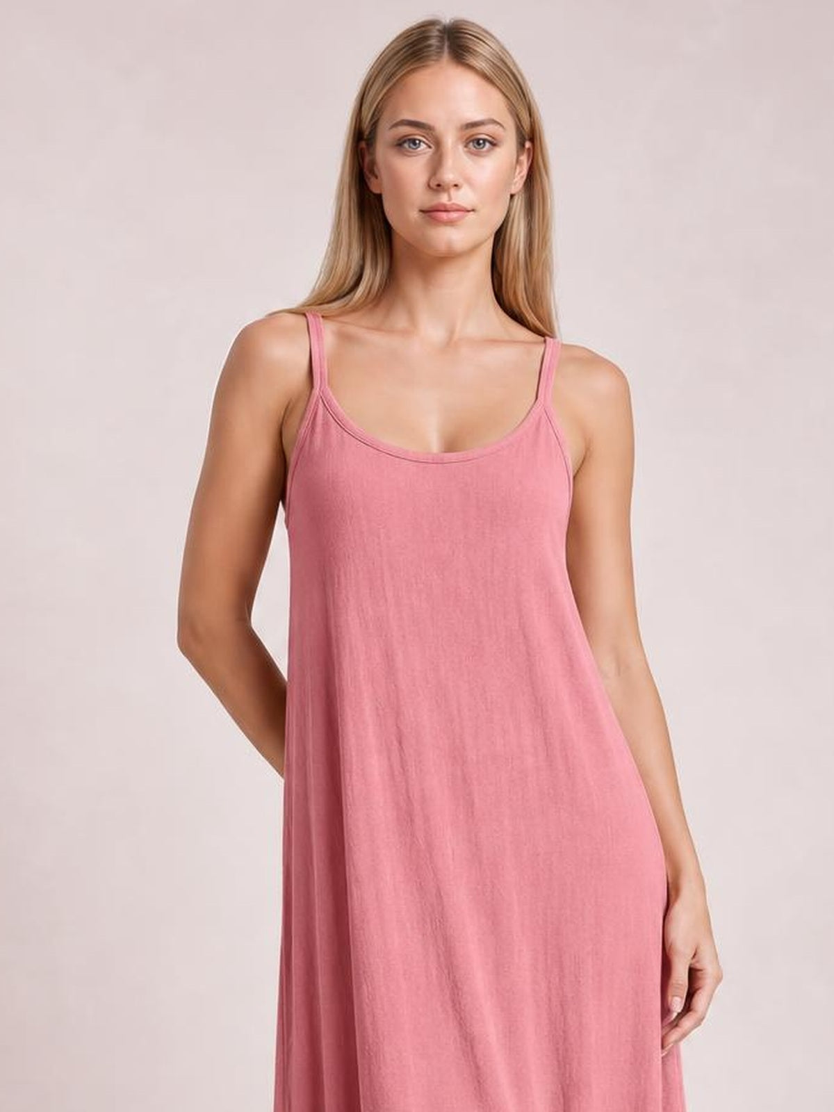 Model poses in a pink scoop neck spaghetti strap maxi dress with a relaxed, flowing silhouette and one hand resting behind her back.