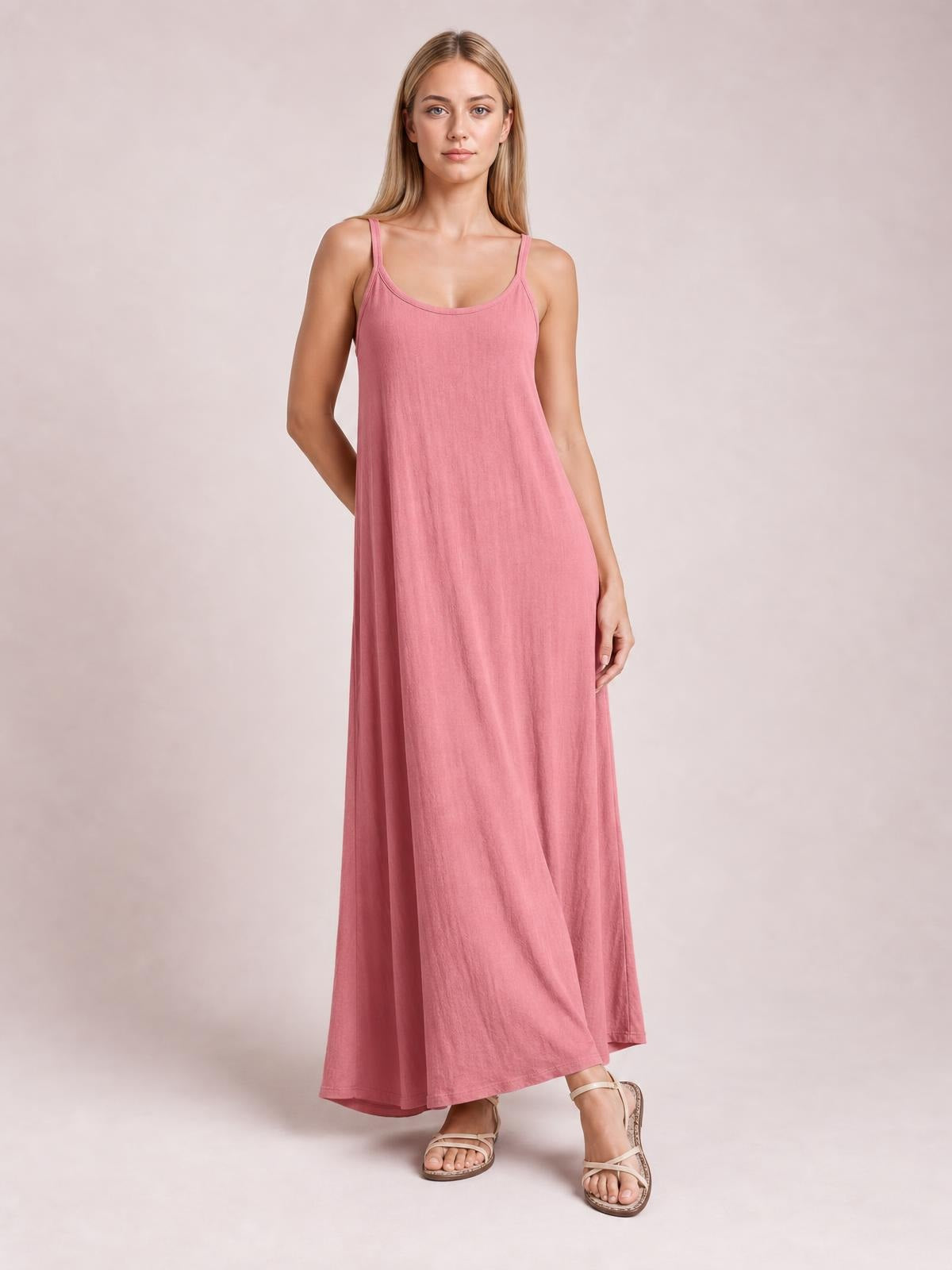 Model poses in a pink scoop-neck spaghetti-strap maxi dress with a relaxed, flowing silhouette and long hem.