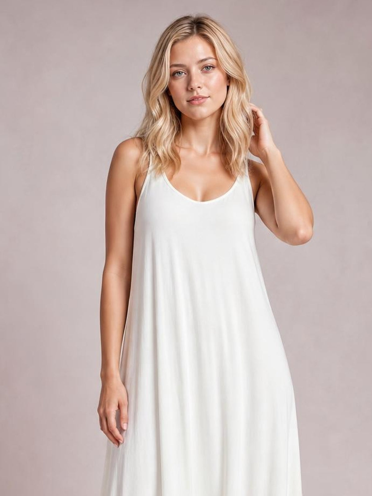 A model poses in a white scoop-neck spaghetti-strap maxi dress with a flowing A-line silhouette and soft, unlined construction.