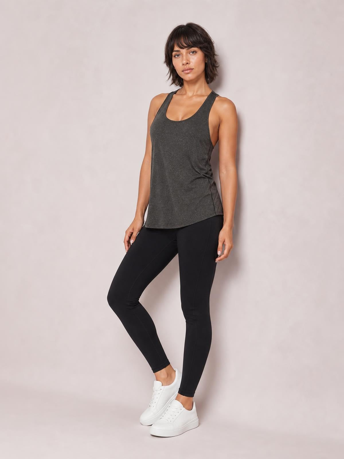 Model wearing a charcoal scoop neck wide strap active tank with a relaxed, slightly curved hem and moderate stretch, posed in black leggings with one knee bent.