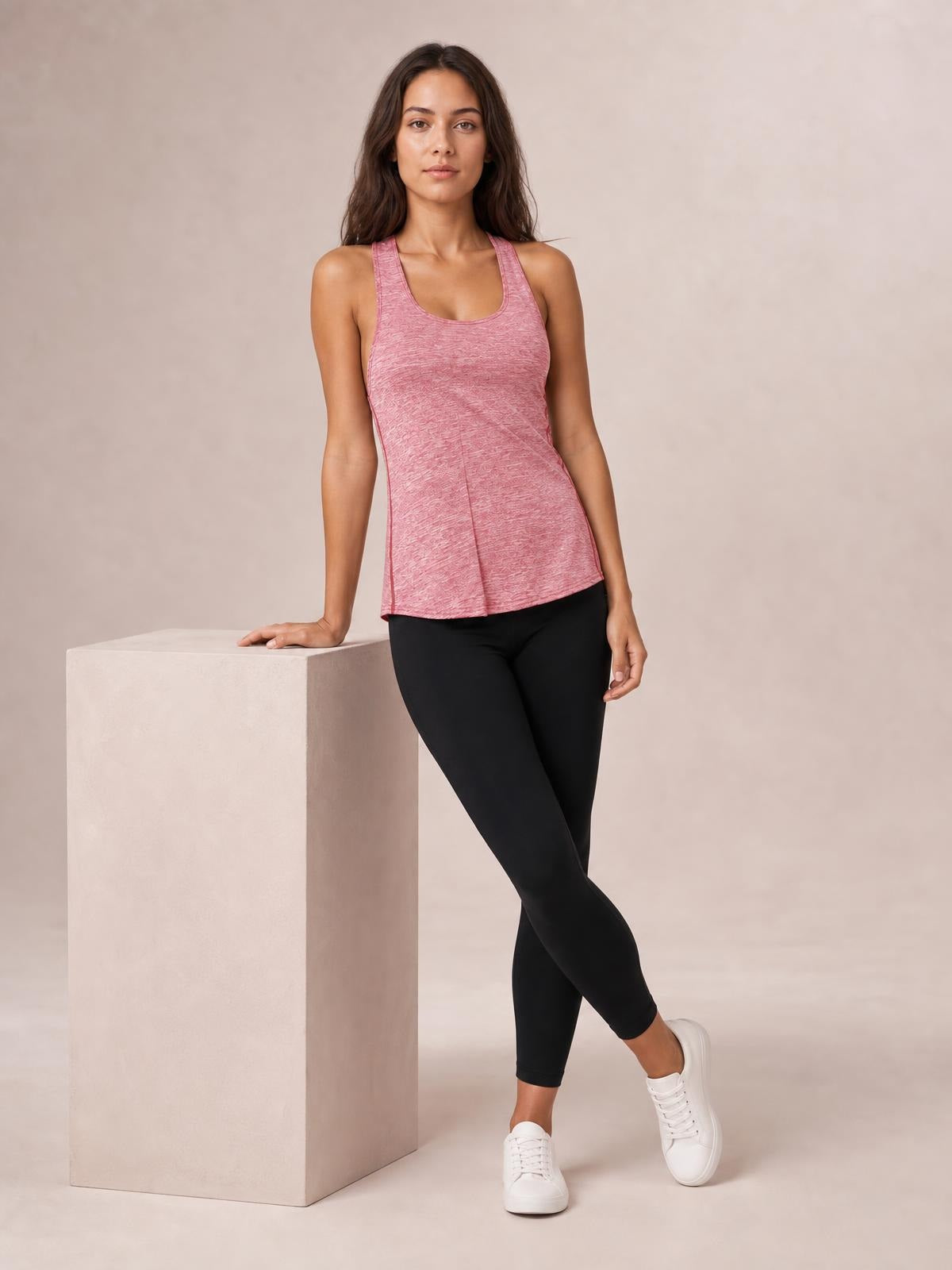 A model wears a pink scoop neck wide strap active tank with a relaxed, slightly flared silhouette, leaning with one hand on a pedestal.