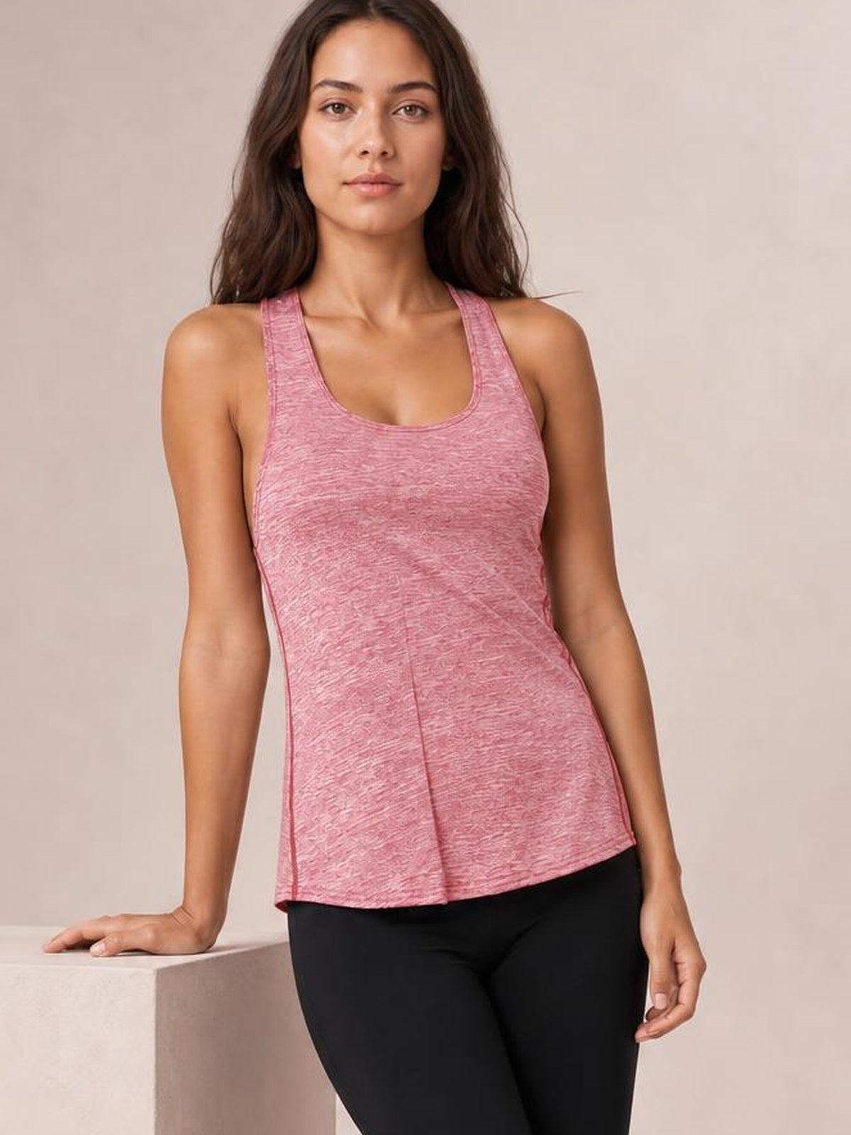 Model wears a pink scoop neck active tank with wide straps, a fitted silhouette, textured fabric, and a gently flared hem over black leggings.