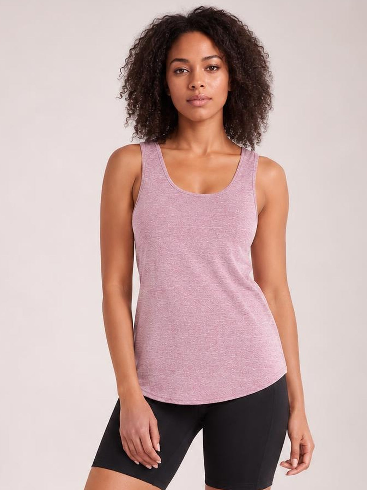 Model wears a mauve scoop neck wide strap active tank with a relaxed curved hem and moderate stretch, paired with black fitted shorts.