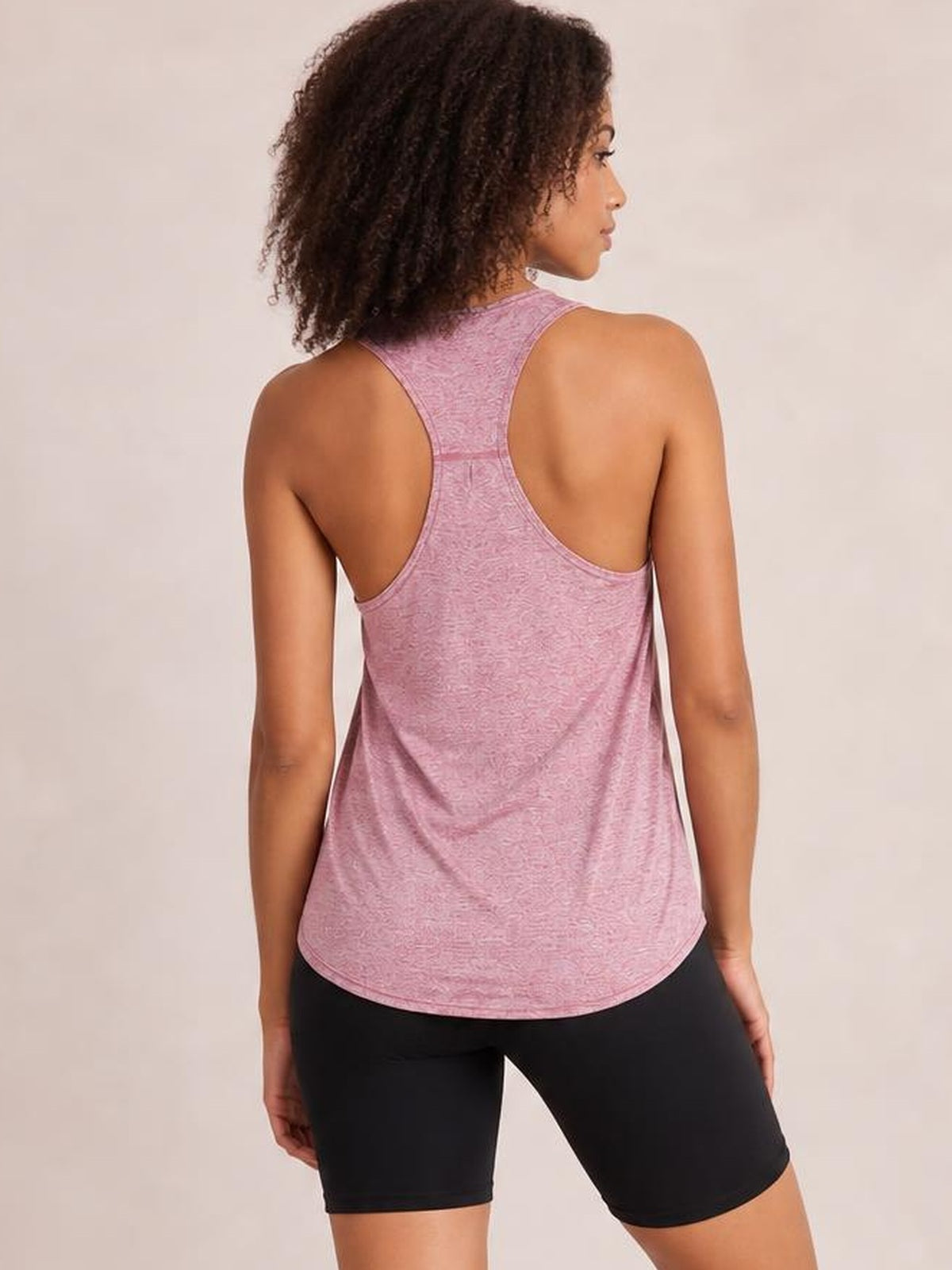 Model shown from behind wearing a pink active tank with wide straps, racerback construction, a relaxed silhouette, and a curved hem.
