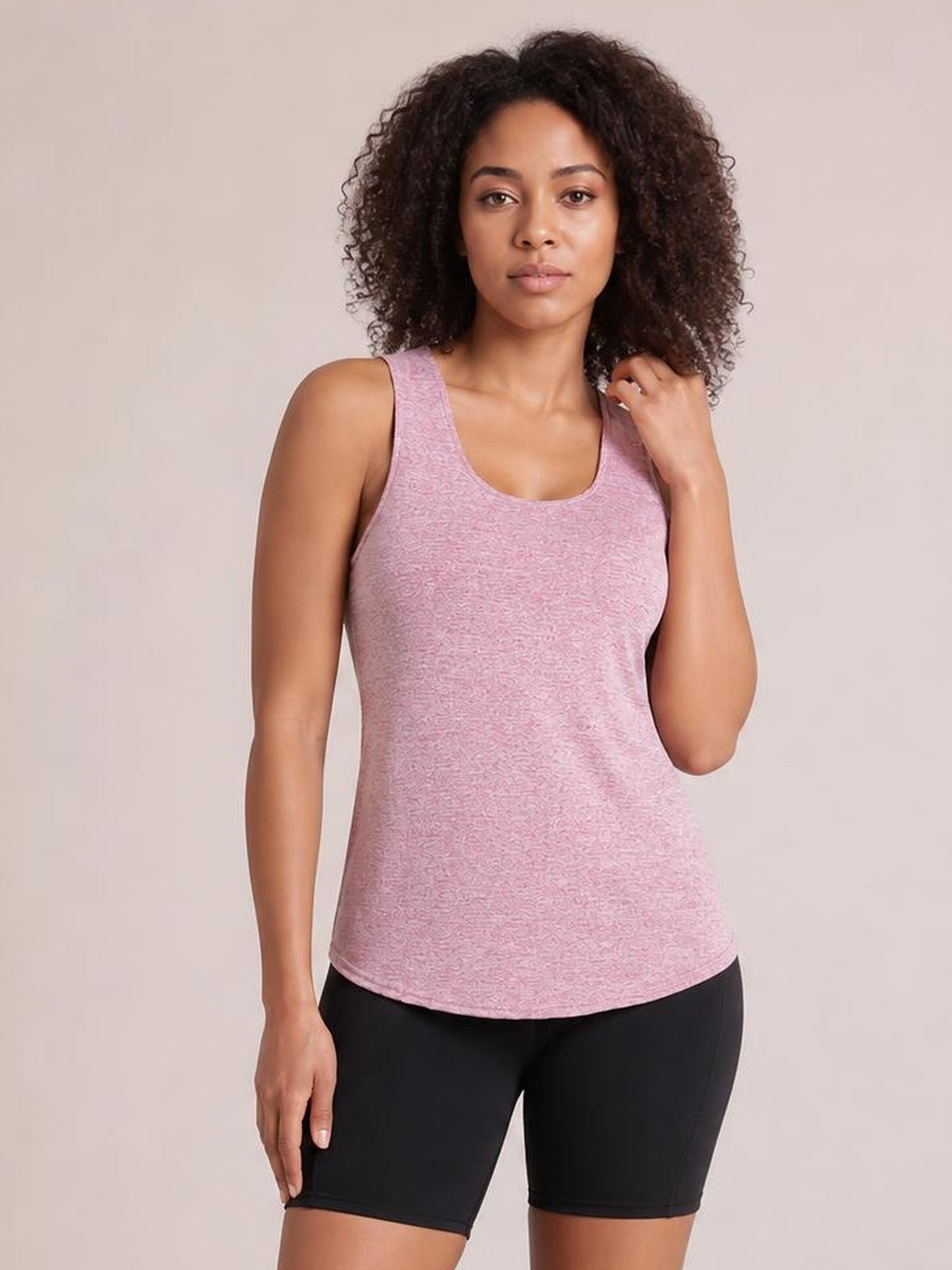 Model poses in a pink scoop neck active tank with wide straps and a gently fitted silhouette, paired with black shorts.