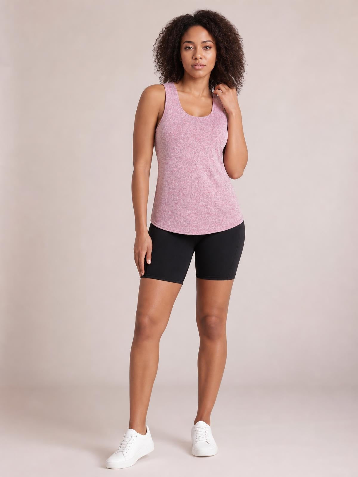 Model wears a pink scoop neck wide strap active tank with a fitted silhouette and curved hem, paired with black workout shorts.