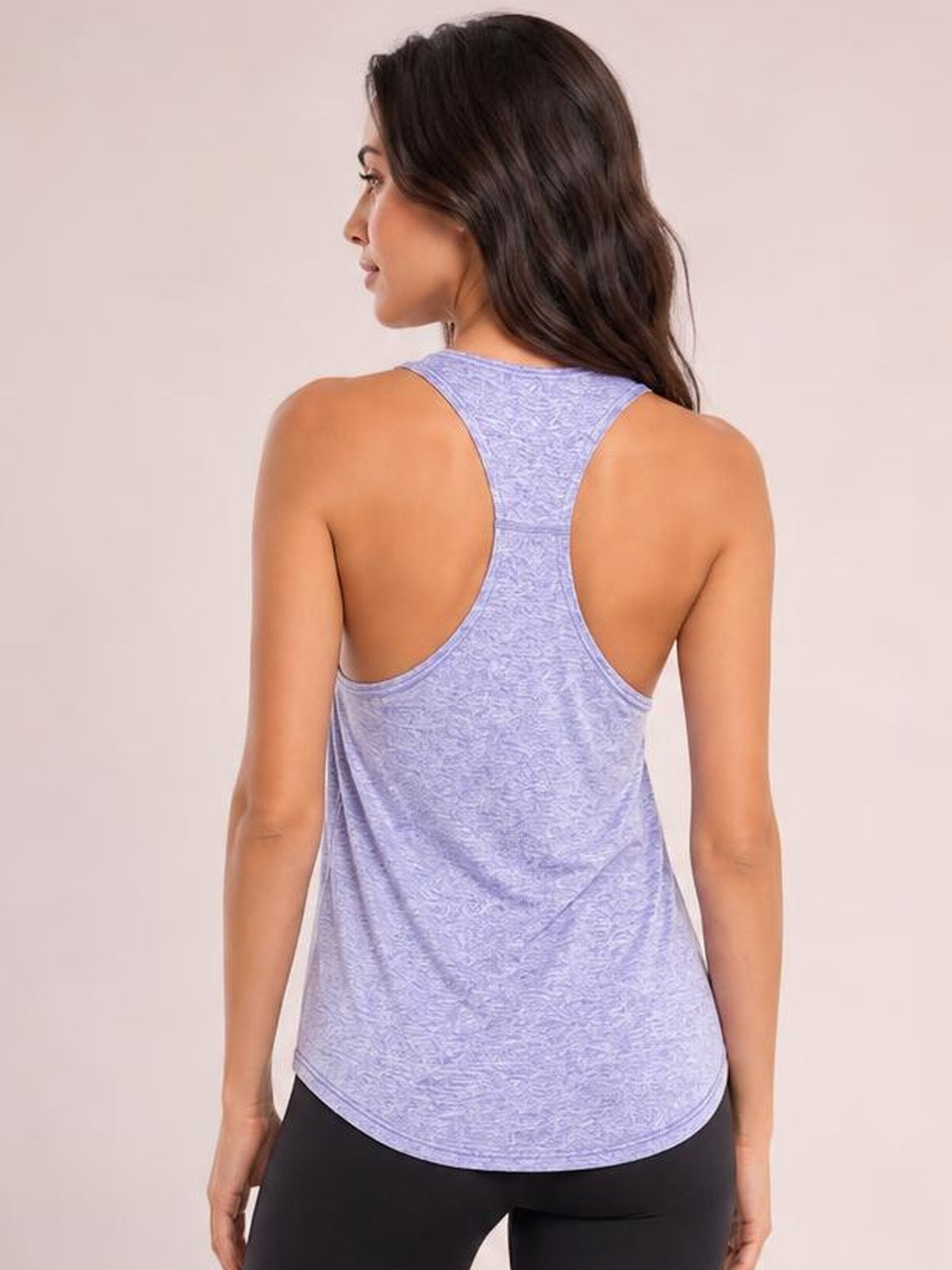 Back view of a model wearing a lavender wide-strap active tank with a racerback construction, relaxed silhouette, and curved hem over black leggings.