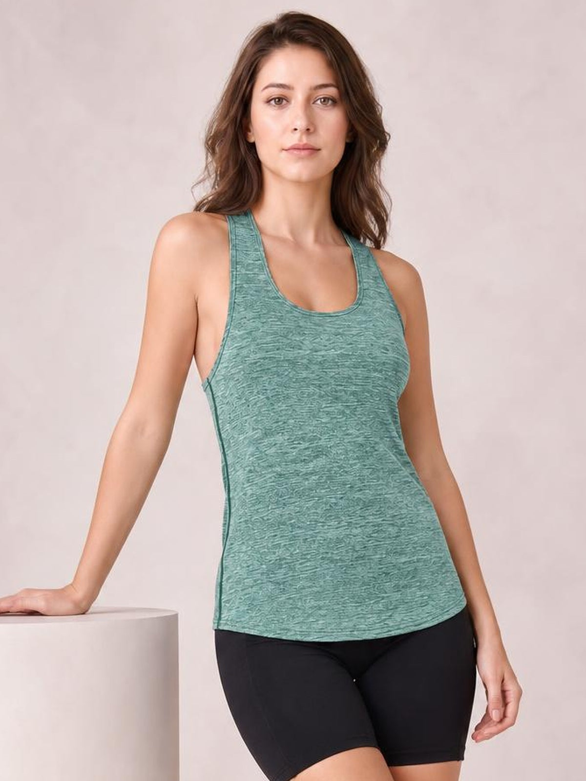 Model poses in a mint green scoop neck active tank with wide straps, a fitted silhouette, and visible side seams, paired with black cycling shorts.