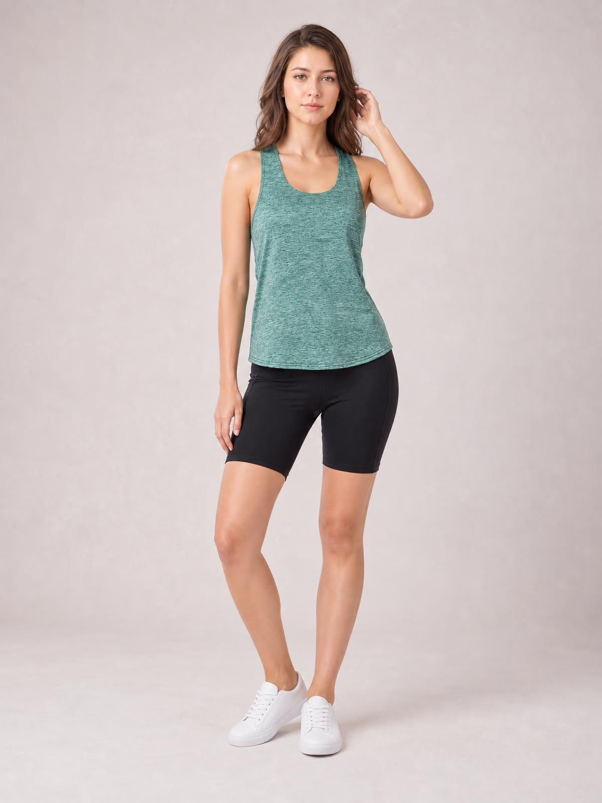 Model wearing a teal scoop neck wide strap active tank with a fitted, gently shaped silhouette and curved hem, paired with black bike shorts.