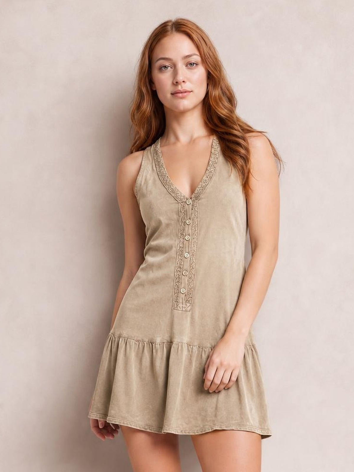 A model poses in a beige sleeveless V-neck mini dress with a relaxed silhouette, decorative button-front placket, embroidered trim, and gathered flounce hem.