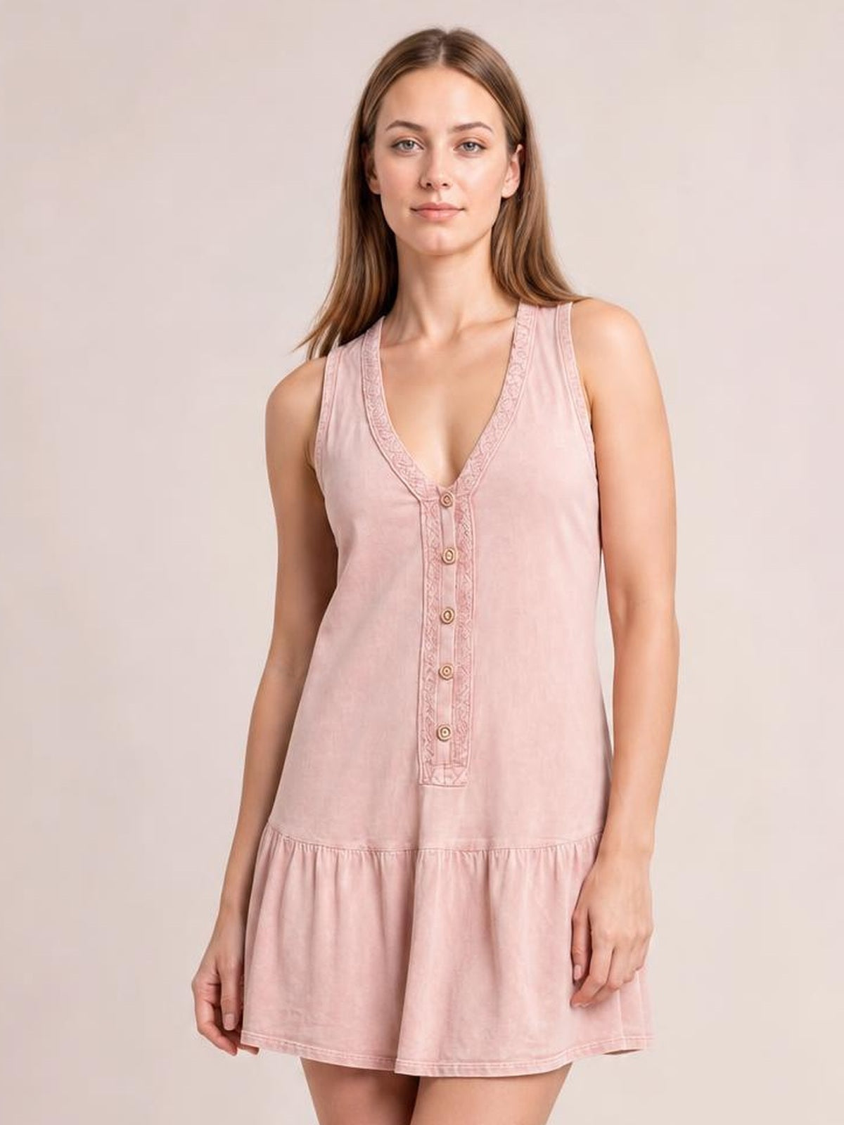 Model wearing a blush pink sleeveless V-neck mini dress with decorative buttons, ruched trim, a relaxed silhouette, and tiered flared hem.