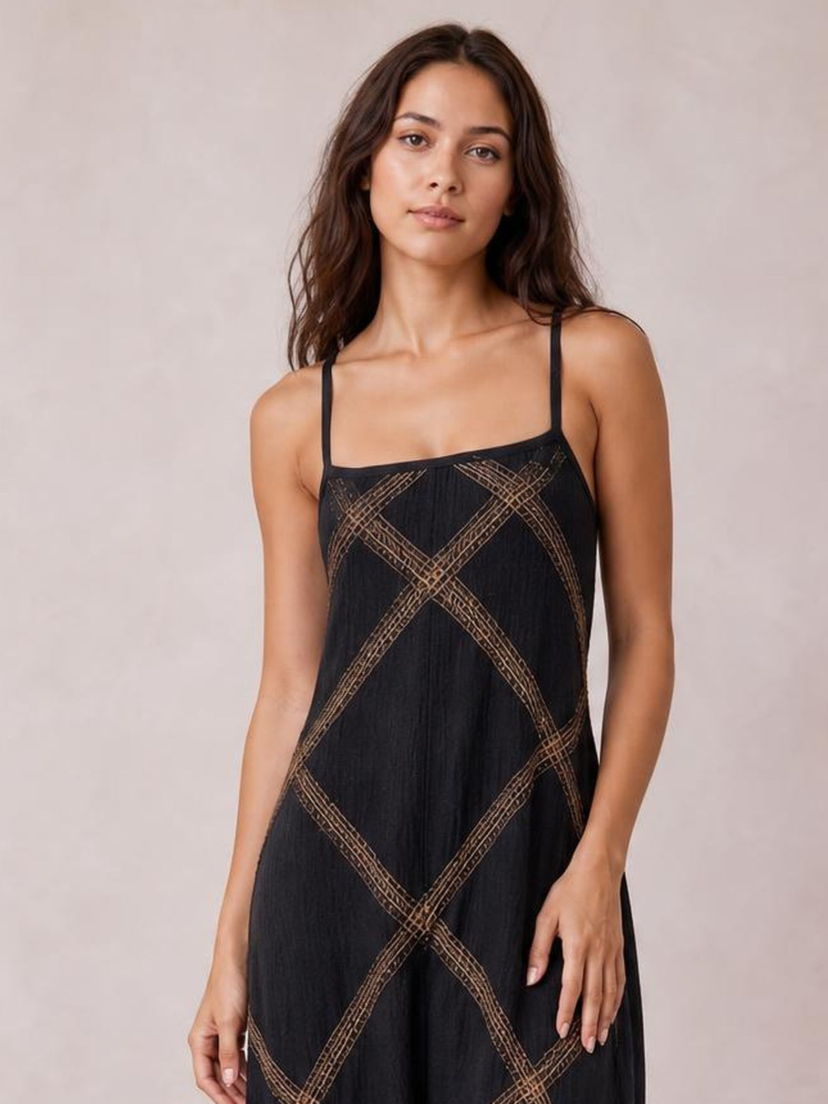 Model wears a black square-neck maxi dress with slender straps, a relaxed flowing silhouette, and contrasting tan geometric line detailing.