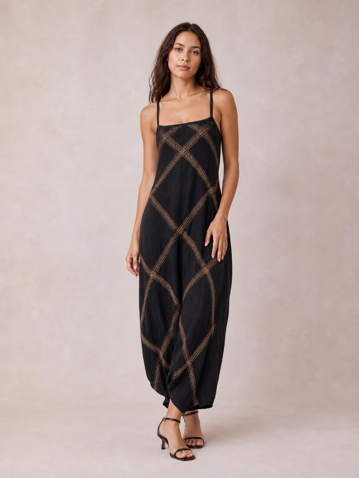 Model wears a black square-neck maxi dress with slim straps, a relaxed flowing silhouette, and contrasting brown geometric line detailing.