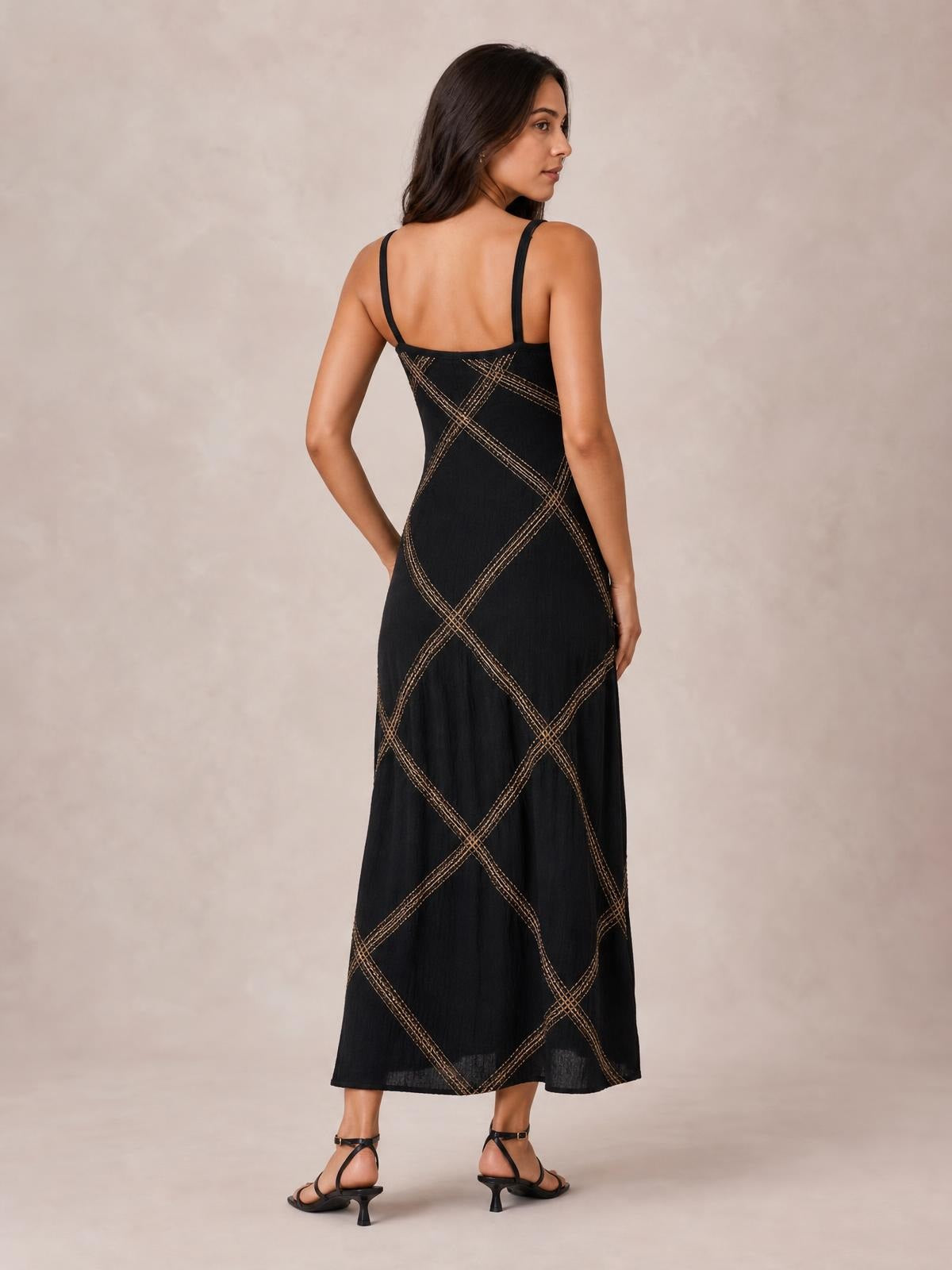 Model shown from the back in a black plus-size maxi dress with thin straps, a flowing long silhouette, and geometric tan contrast stitching.