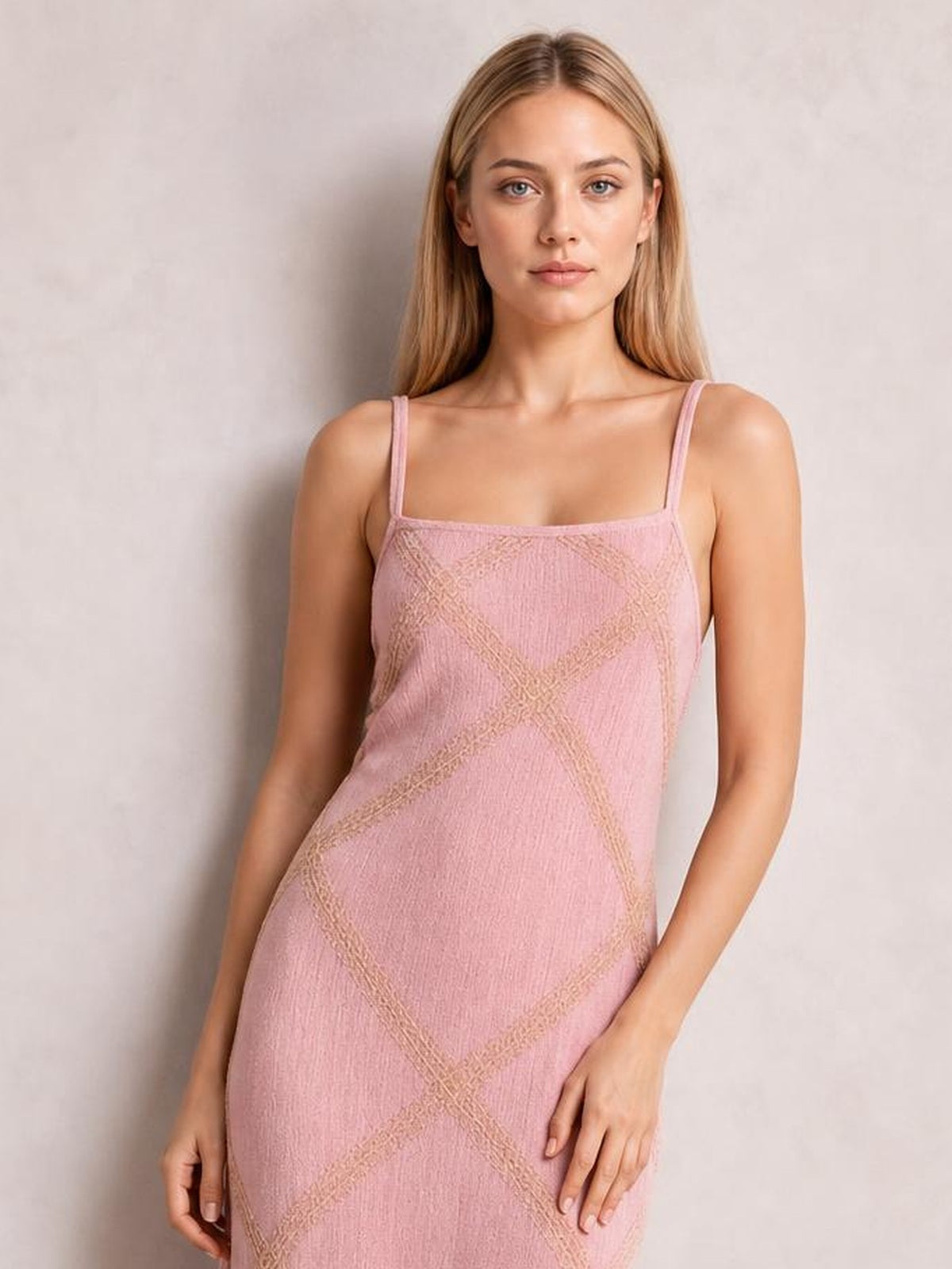 A model stands in a pink square-neck maxi dress with slender shoulder straps and a straight, close-fitting silhouette featuring geometric textured lines.