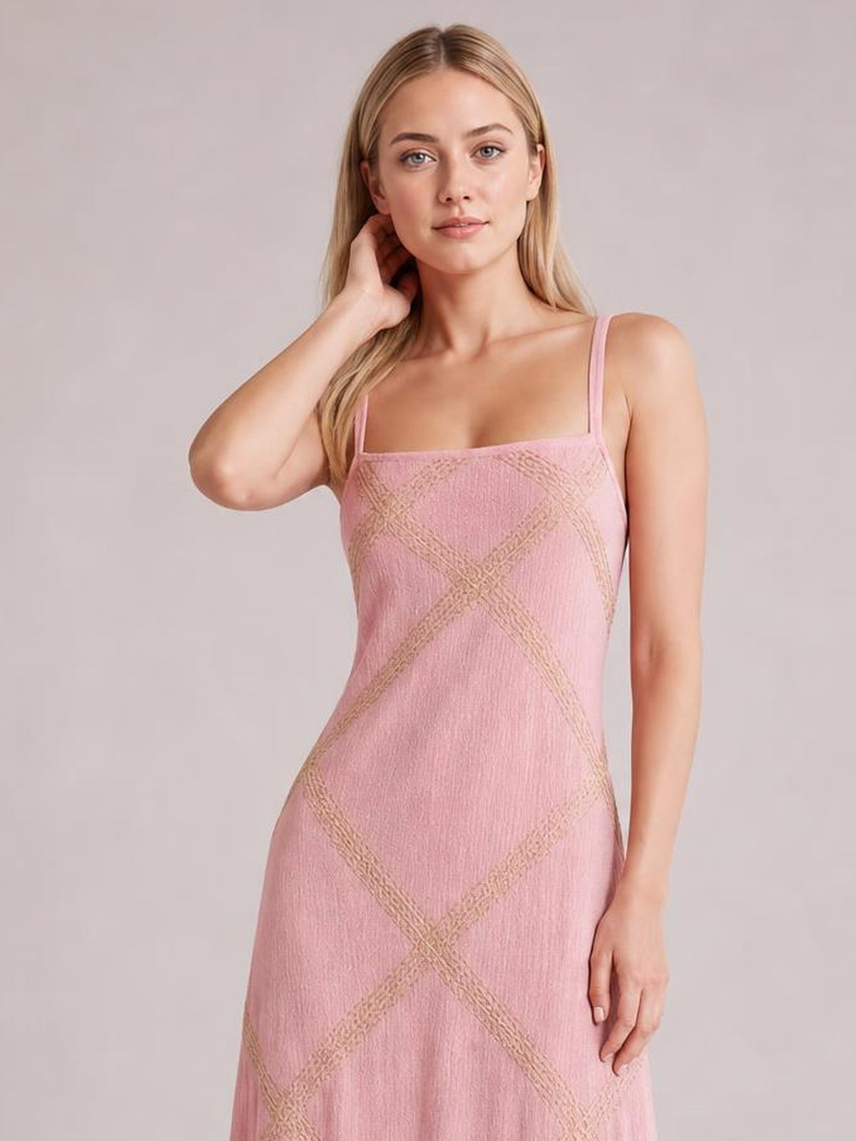 A model poses with one hand at her neck in a pink square-neck maxi dress featuring thin straps, a fitted silhouette, and geometric contrasting bands.