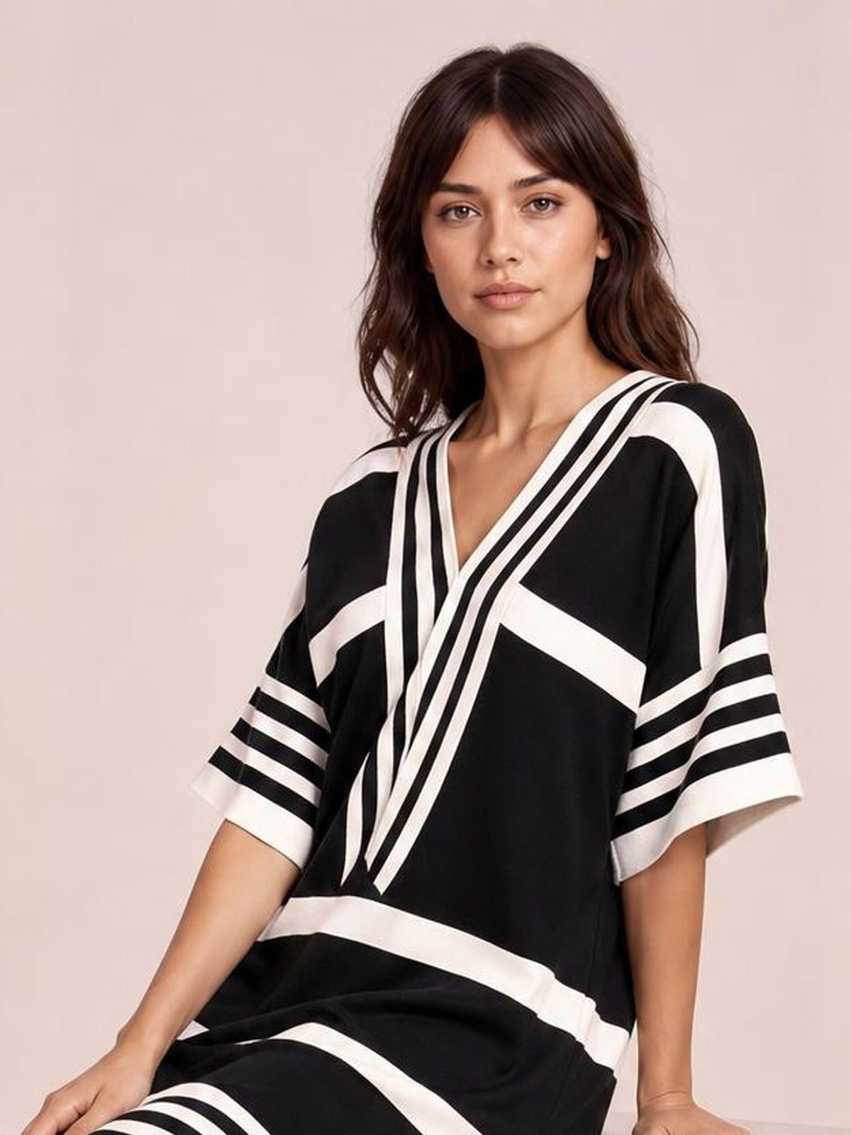 Model seated in a black-and-white striped midi dress with half sleeves, a V-neckline, bold geometric bands, and a relaxed silhouette.