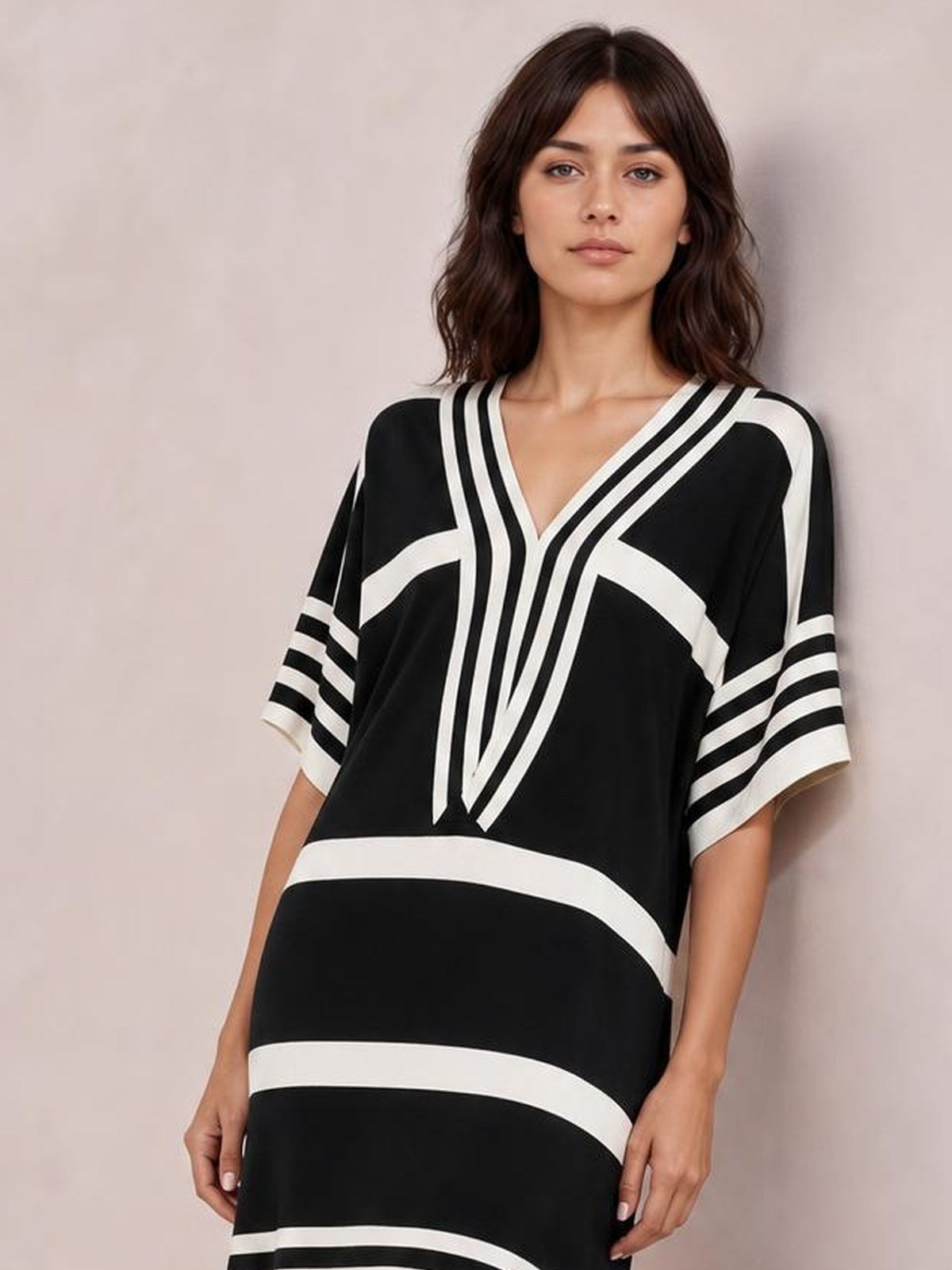 A model stands wearing a black-and-white striped midi dress with half sleeves, a V-neck, bold geometric bands, and a relaxed straight silhouette.