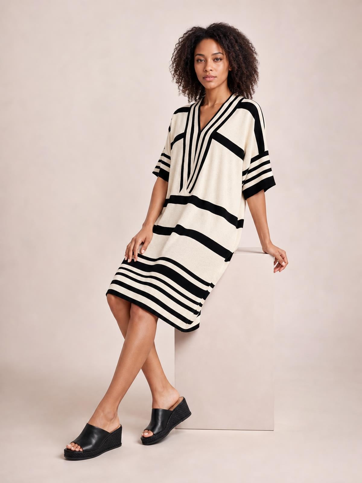 A model poses in a cream and black striped half-sleeve midi dress with a relaxed straight silhouette, V-neck, and contrasting striped hem.