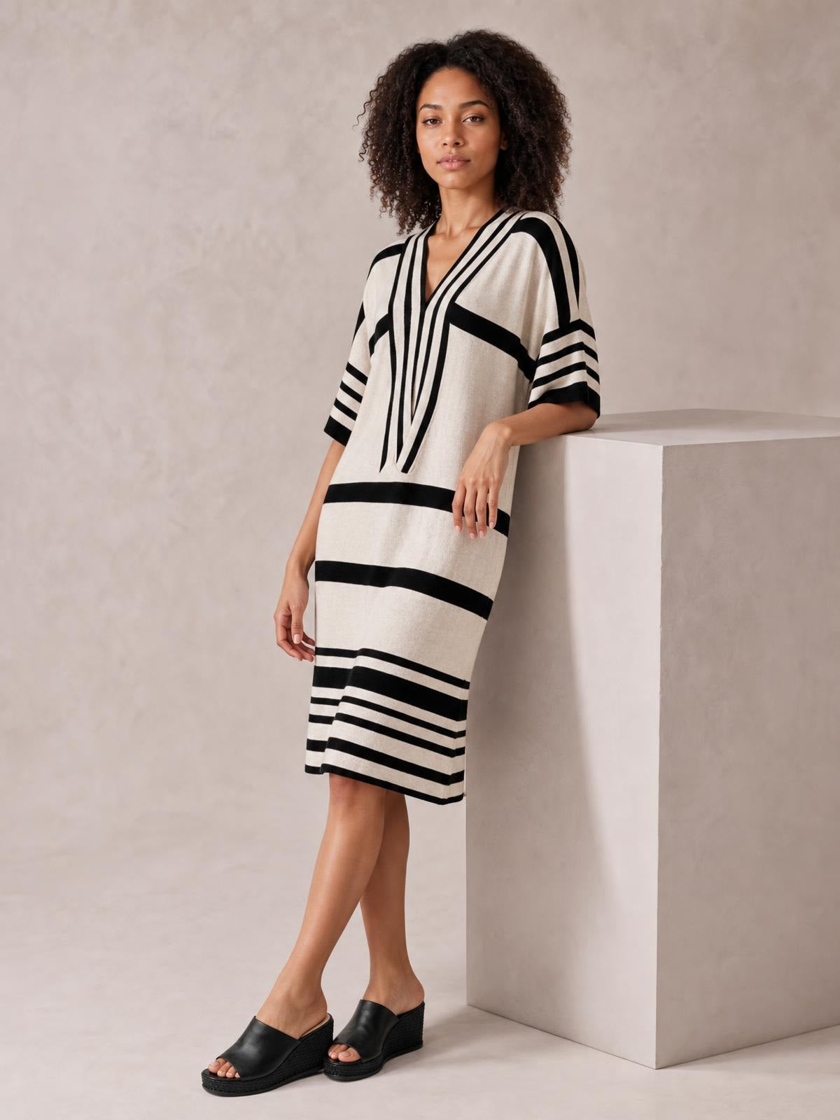 Model wears a cream and black striped half-sleeve midi dress with a V-neck, relaxed straight silhouette, and contrasting horizontal and diagonal bands.