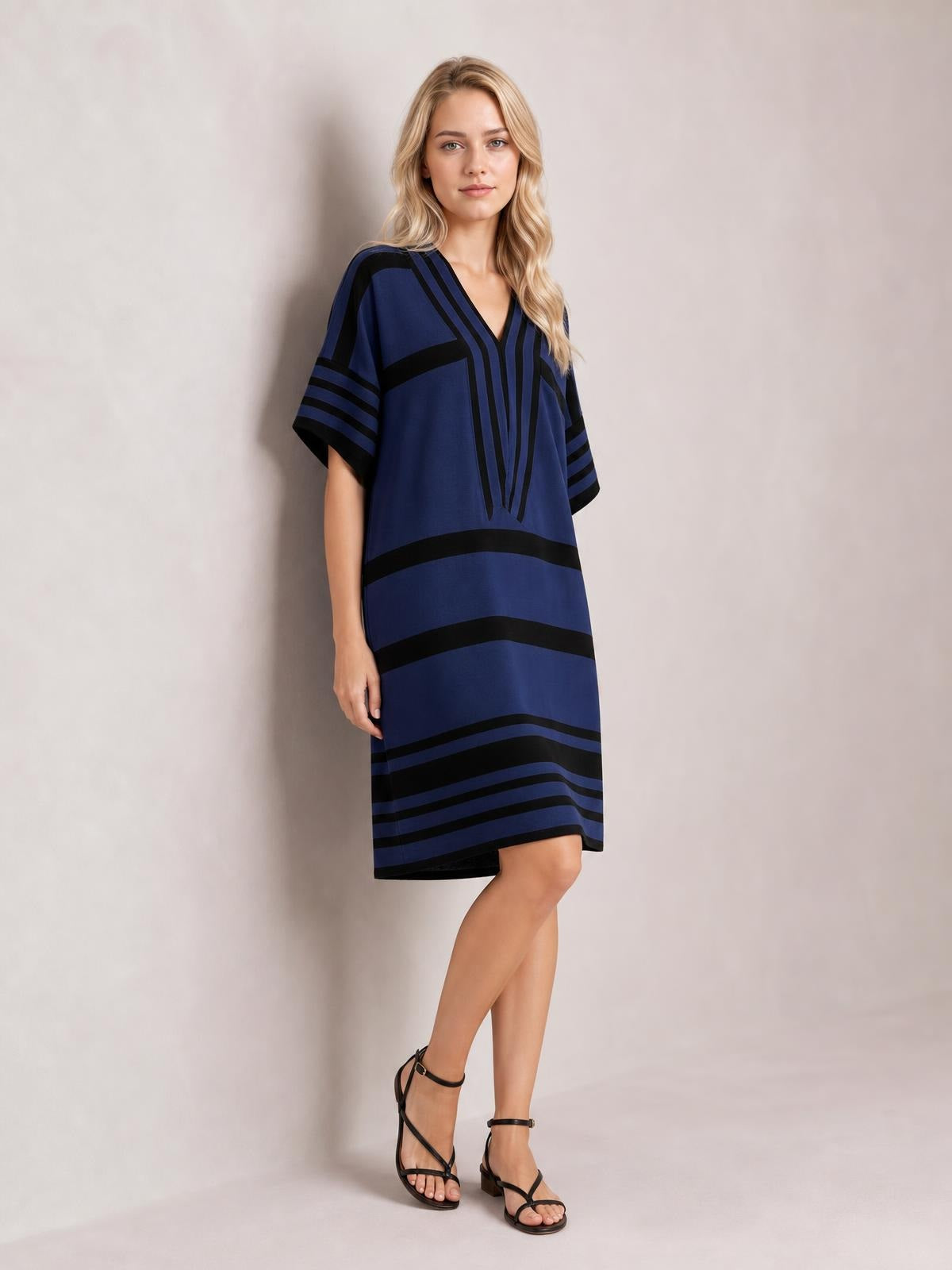 A model poses with crossed legs in a navy and black striped half-sleeve midi dress featuring a relaxed straight silhouette and V-neckline.