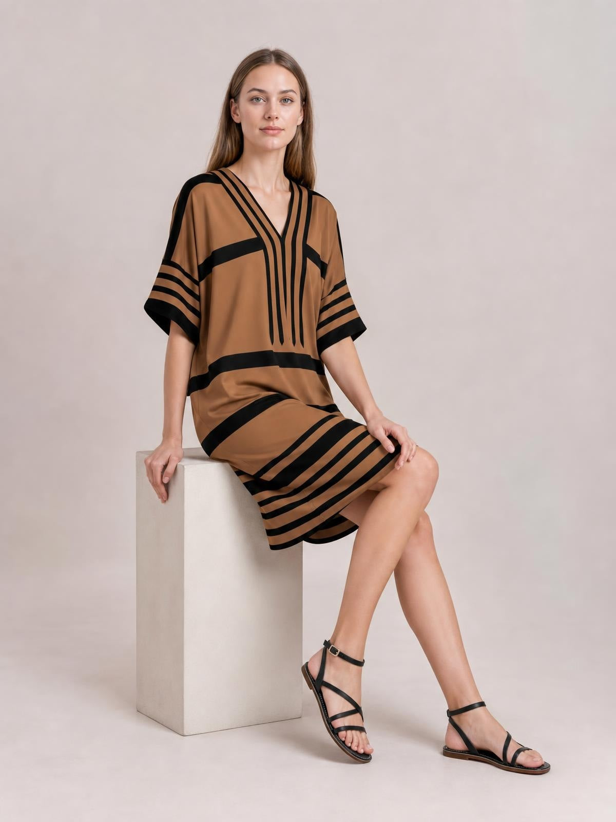A model sits in a brown and black striped midi dress with a V-neck, relaxed silhouette, bold contrast bands, and loose half sleeves.