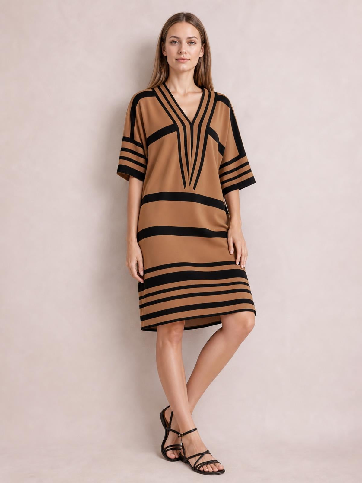 Model wears a camel-brown striped half-sleeve midi dress with black contrast bands, V-neckline, relaxed straight silhouette, and crossed legs.