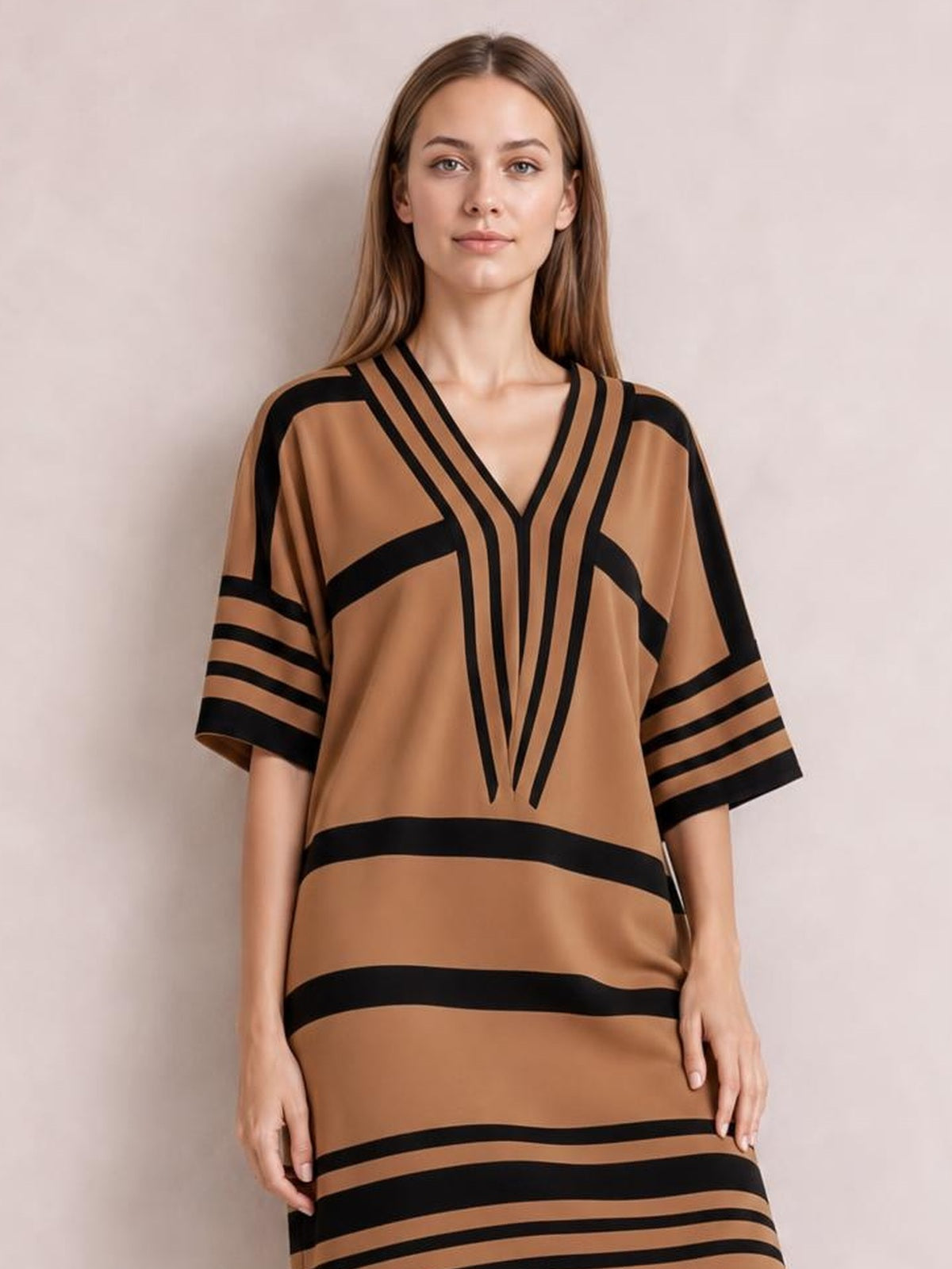 A model stands in a brown and black striped midi dress with a V-neck, half sleeves, bold geometric trim, and a relaxed straight silhouette.
