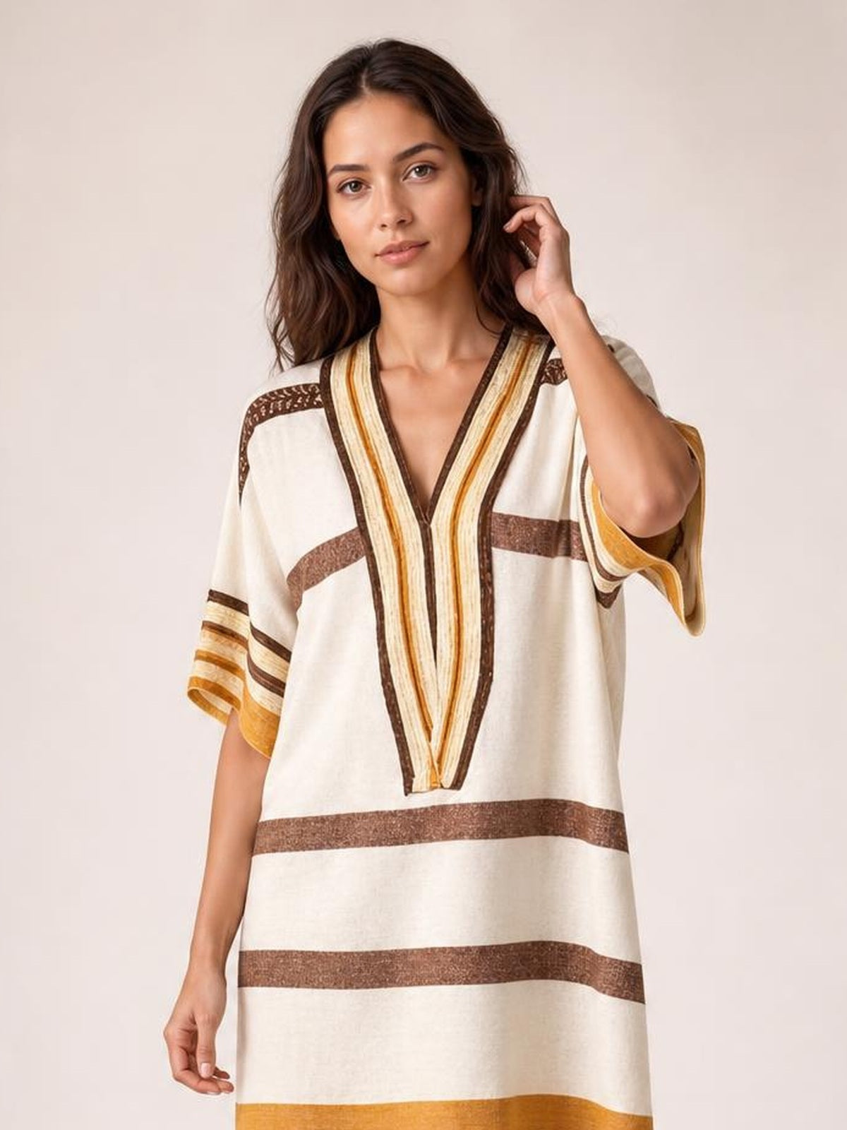 Model poses in a relaxed cream striped midi dress with brown and mustard bands, a V-neckline, loose half sleeves, and an easy straight silhouette.