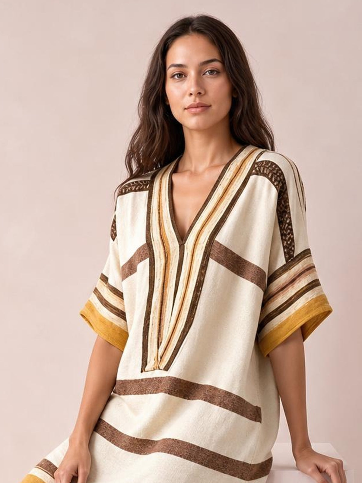 A model wears a cream striped half-sleeve midi dress with brown and mustard accents, a relaxed silhouette, and a deep V-neckline while seated.