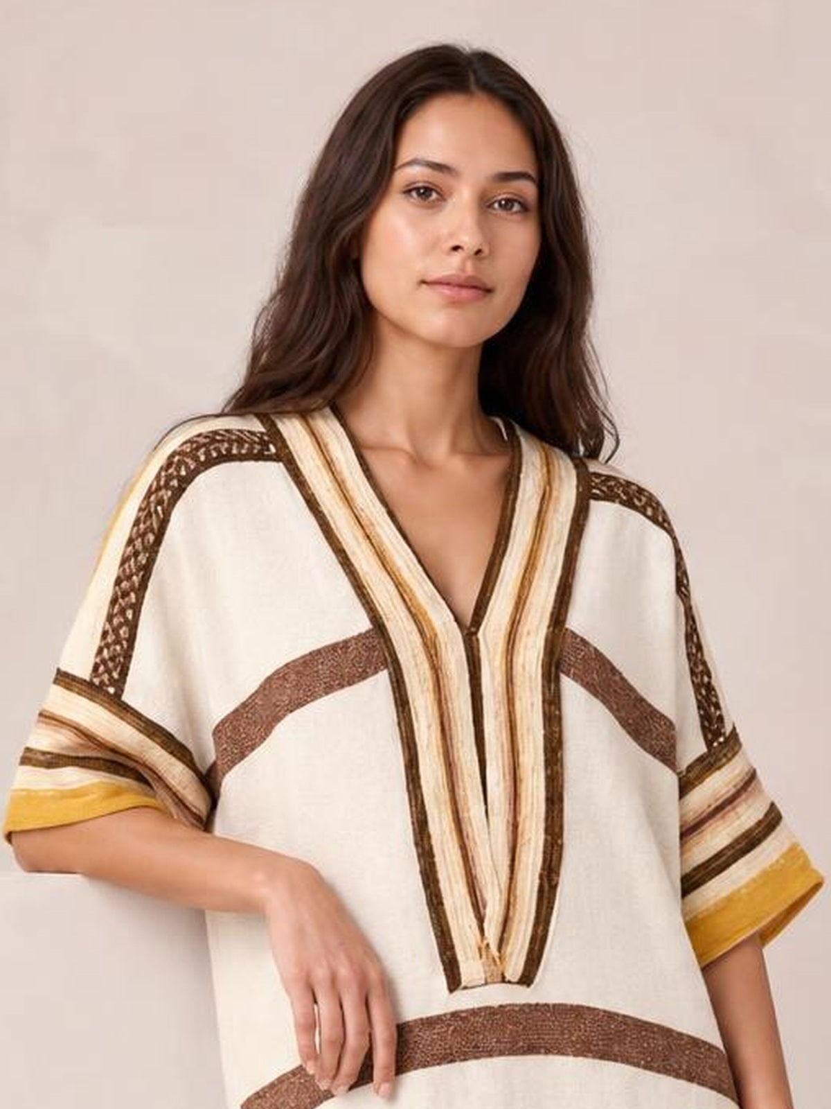 Model poses in a cream striped dress with a deep V-neck, loose silhouette, contrasting brown and mustard bands, and relaxed half sleeves.