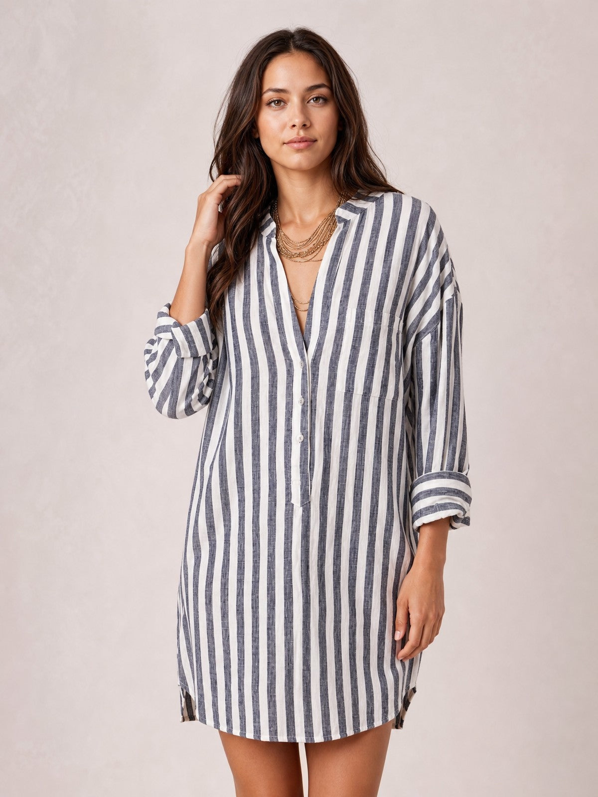 A model poses in a navy-and-white striped shirt mini dress with a relaxed silhouette, button front, chest pocket, long rolled sleeves, and above-knee hem.