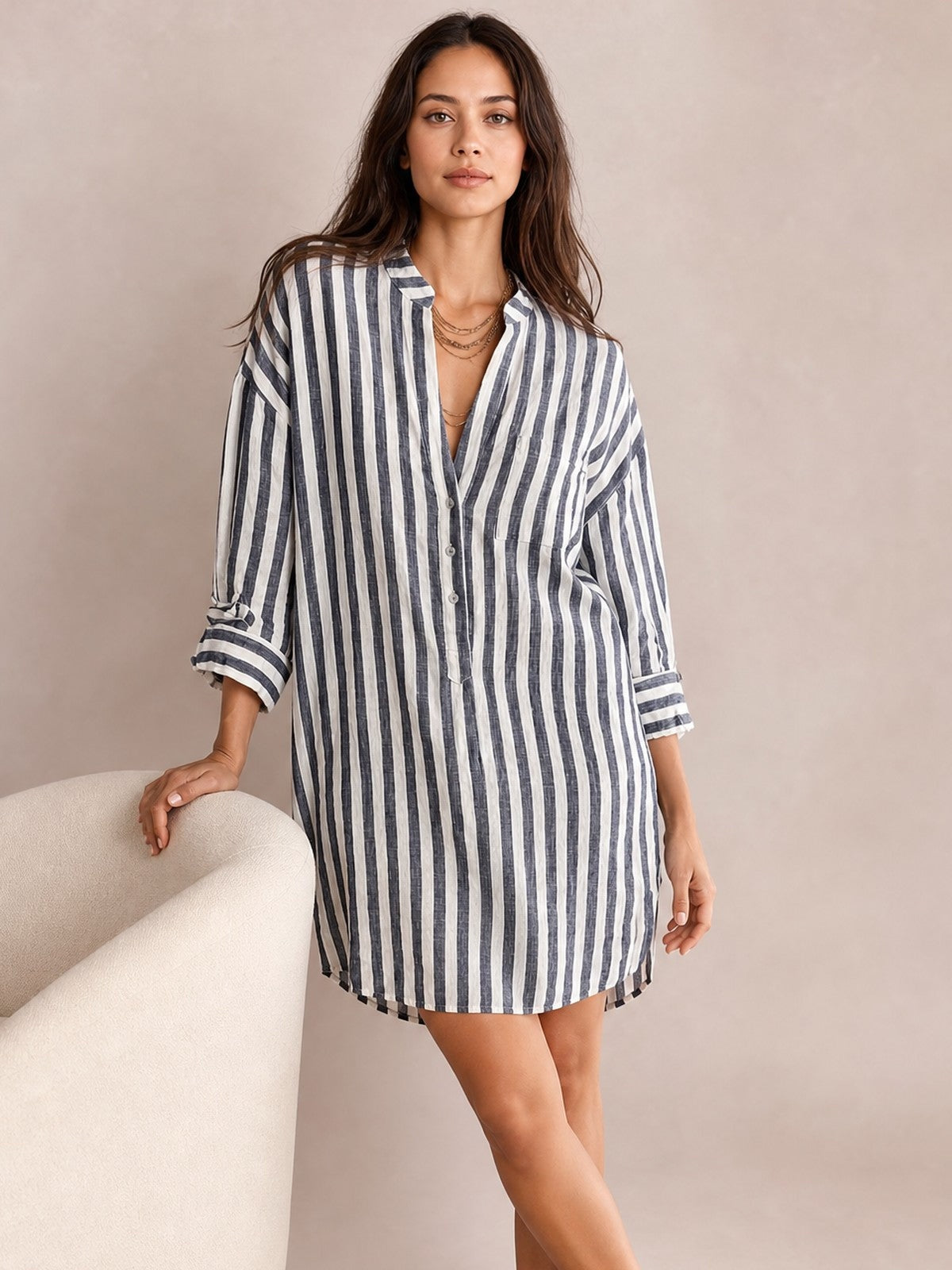 Model poses in a relaxed navy-and-white striped linen shirt mini dress with a loose silhouette, buttoned front, chest pocket, long sleeves, and rolled cuffs.