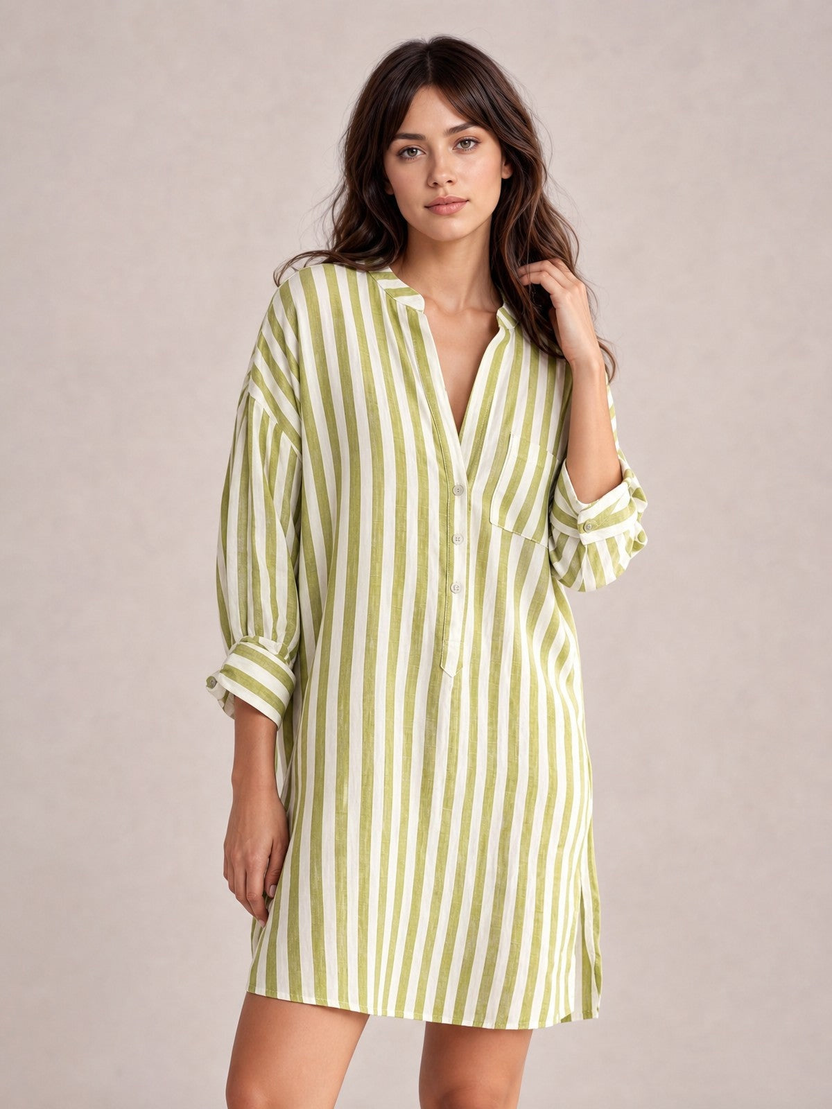 Model poses in a green-and-white striped linen shirt mini dress with a relaxed silhouette, buttoned front, chest pocket, seam details, and rolled long sleeves.