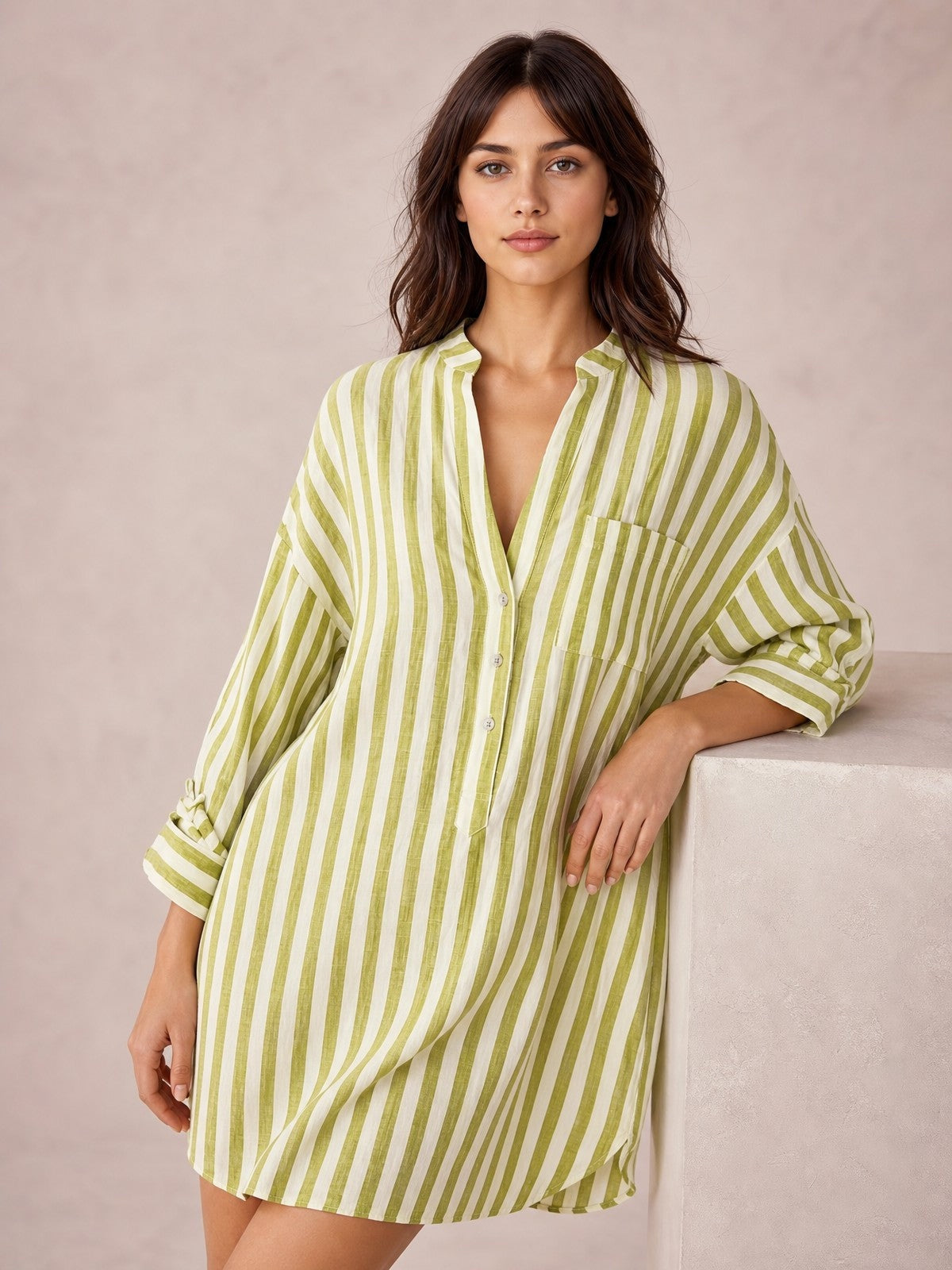 Model wears a relaxed striped linen shirt mini dress in olive green and white with long sleeves, button front, chest pocket, seam detail, and curved above-the-knee hem.