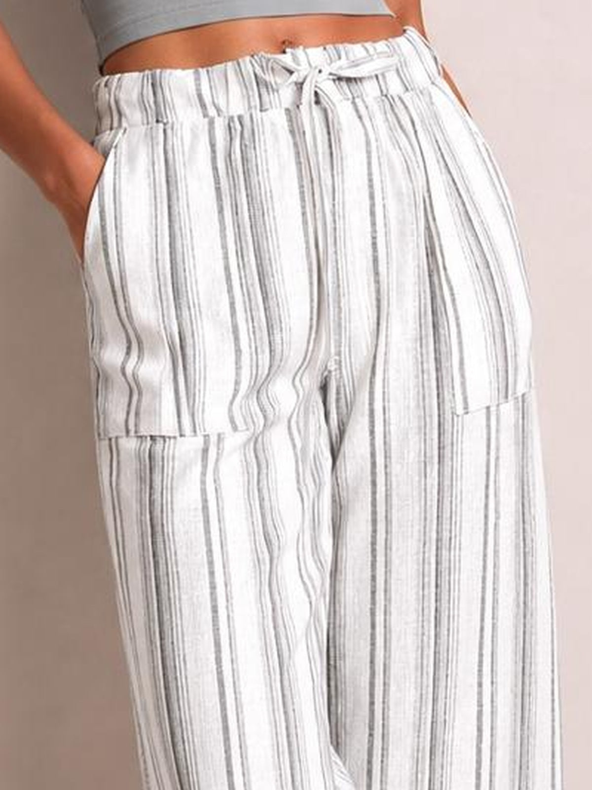 Close-up of a model wearing white striped wide leg pants with a drawstring elastic waistband, side pockets, and a relaxed flowing silhouette.
