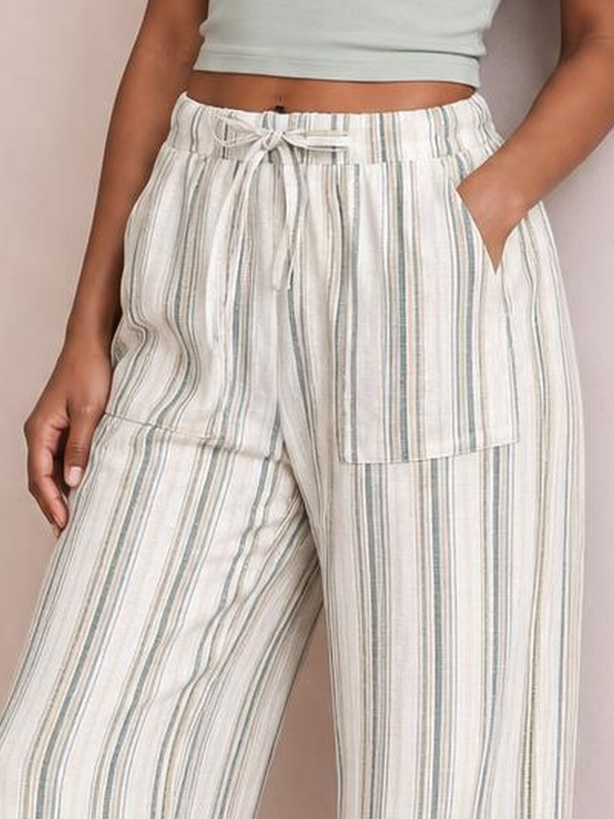 A model wears cream striped wide-leg pants with multicolor vertical lines, an elastic drawstring waist, and visible side pockets.