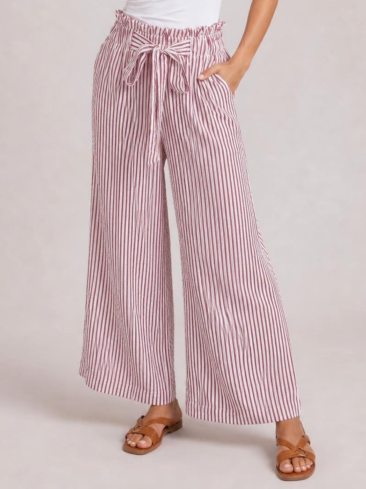 Model wearing pink-and-white striped wide-leg paper bag pants with a tied waist and side pockets, posing with one hand tucked into a pocket.