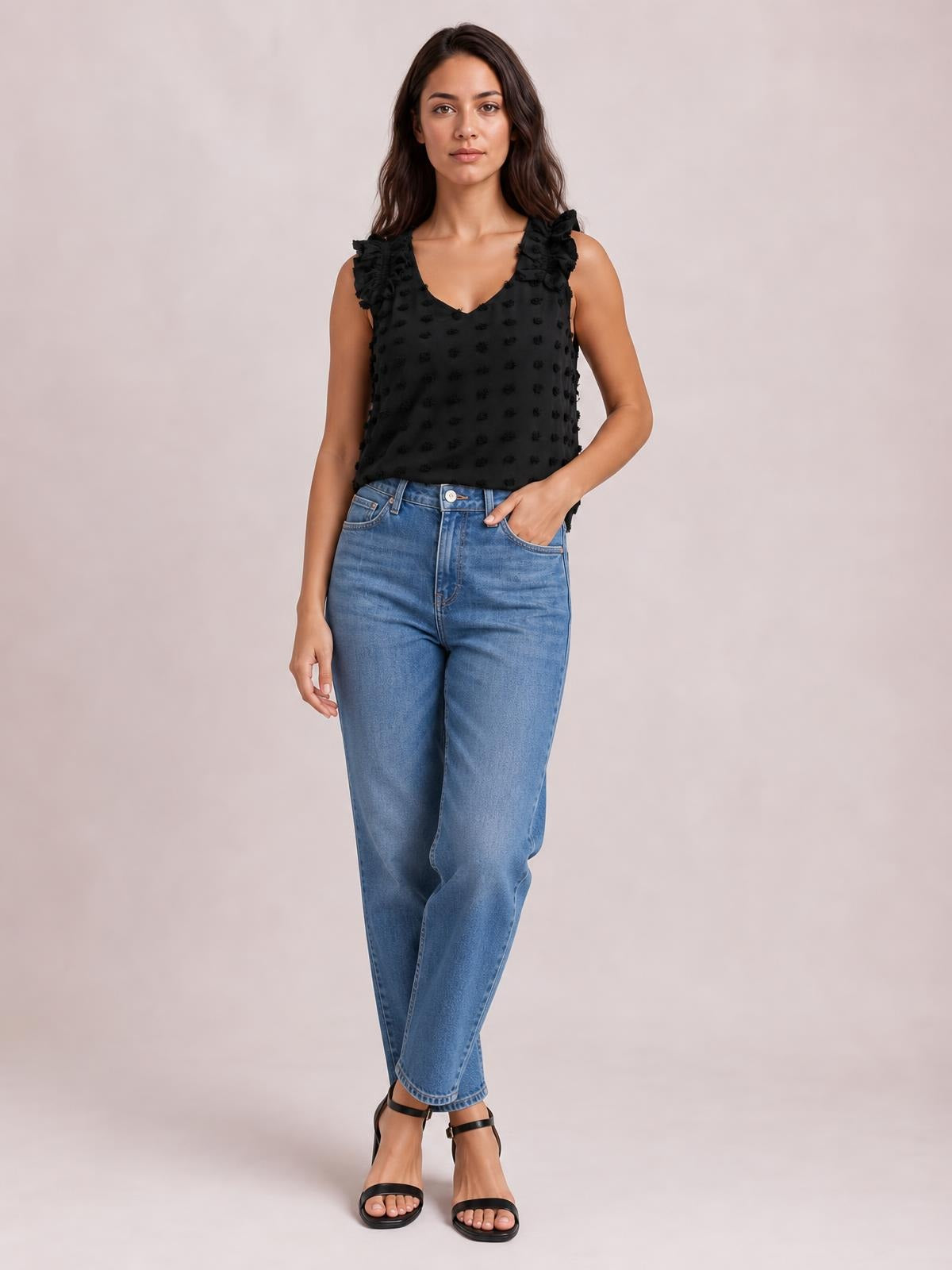 Model wearing a black Swiss dot V-neck tank with ruffled shoulder straps, a relaxed straight silhouette, and high-waisted blue jeans.