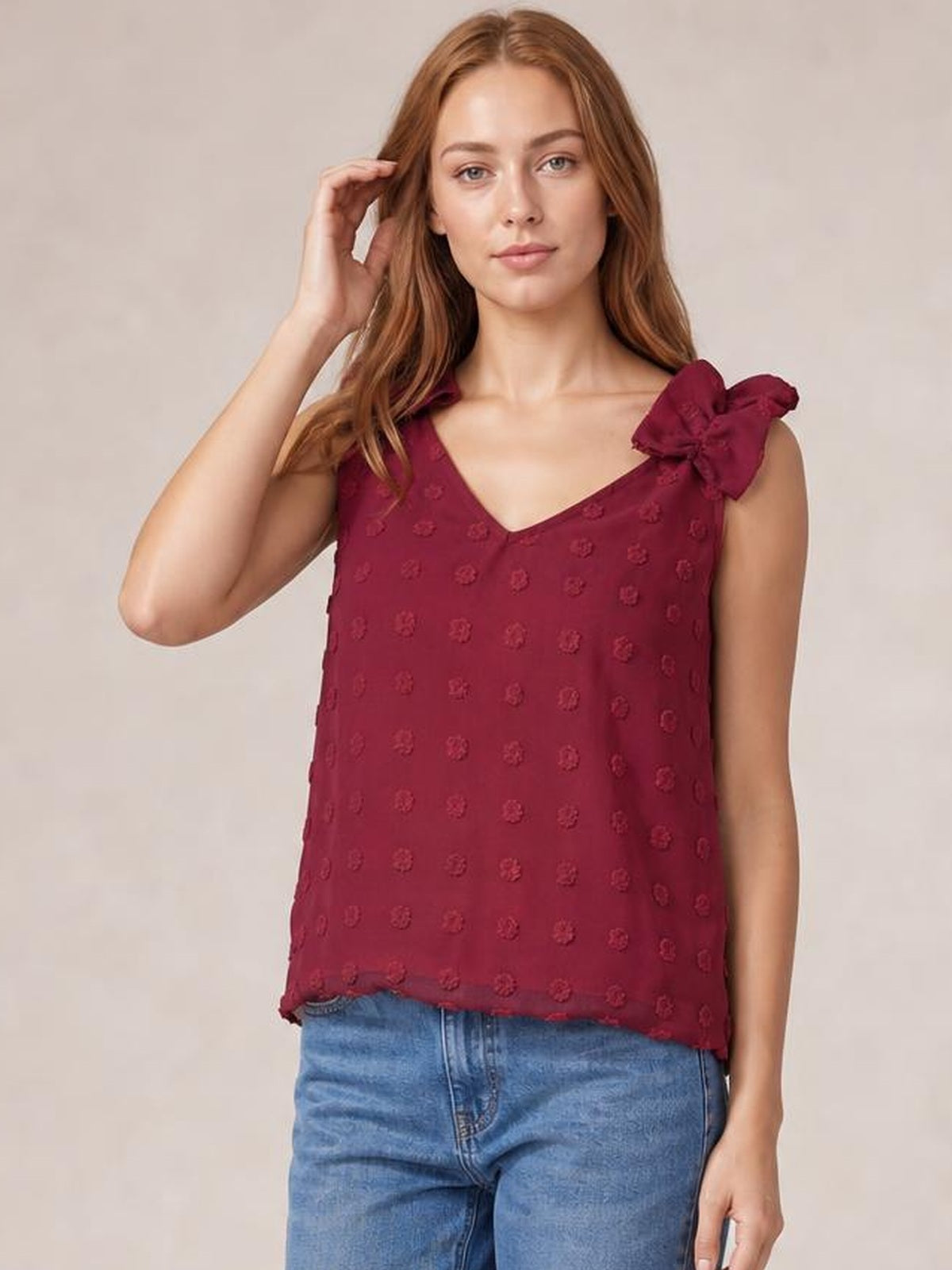 Model wearing a burgundy Swiss dot V-neck tank with a relaxed straight silhouette, textured dots, bow shoulder detail, and softly scalloped hem.
