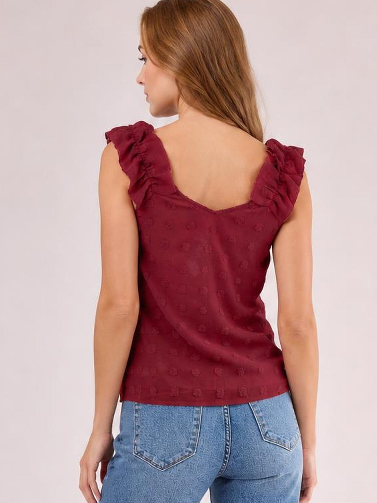 Model turned away in a burgundy Swiss dot tank with ruffled shoulder straps, a low back neckline, and a fitted silhouette.
