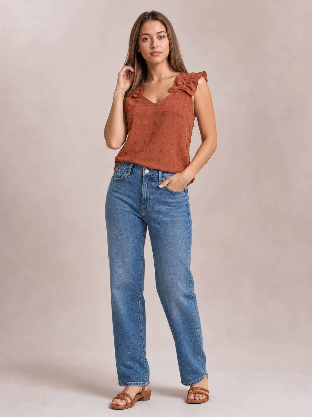 Model wears a rust Swiss dot V-neck tank with ruffled shoulder straps and a relaxed silhouette, posing with one hand in her jeans pocket.