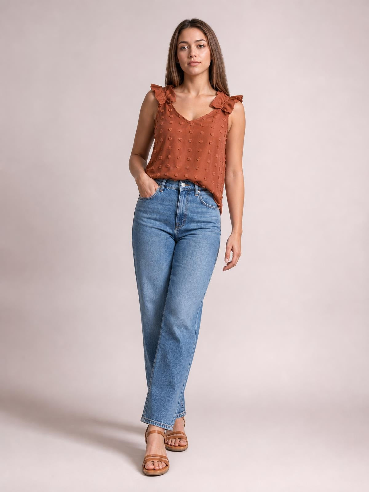 A model wears a rust Swiss dot V-neck tank with ruffled shoulder straps and a relaxed straight silhouette, paired with jeans and one hand in a pocket.