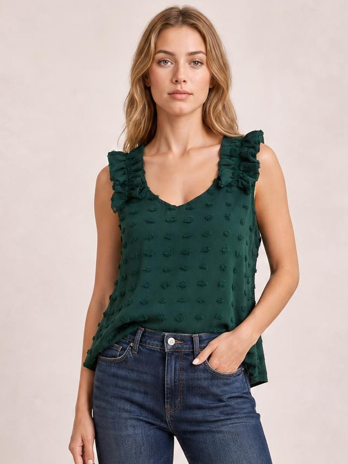 Model wearing a dark green Swiss dot V-neck tank with ruffled shoulder straps and a relaxed, straight silhouette, standing with one hand in her jeans pocket.