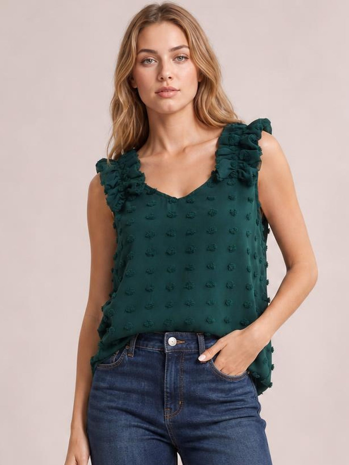 Model wears a dark teal Swiss dot V-neck tank with ruffled shoulder straps and a relaxed silhouette, posing with one hand in her jeans pocket.