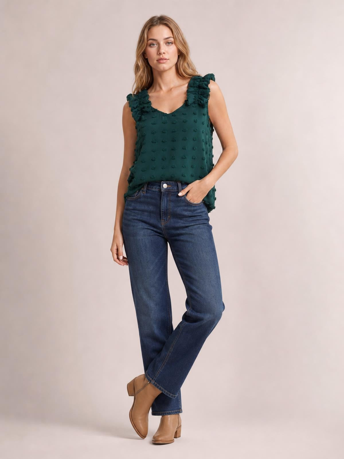 A model poses with one hand in her jeans pocket, wearing a deep teal Swiss dot V-neck tank with a relaxed silhouette and ruffled shoulder straps.