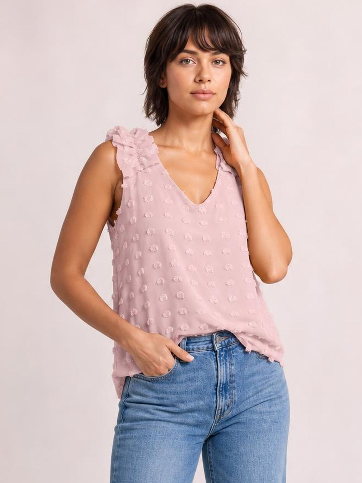 Model poses in a pink Swiss dot V-neck tank with ruffled shoulder straps, a relaxed silhouette, and a softly flowing hem.